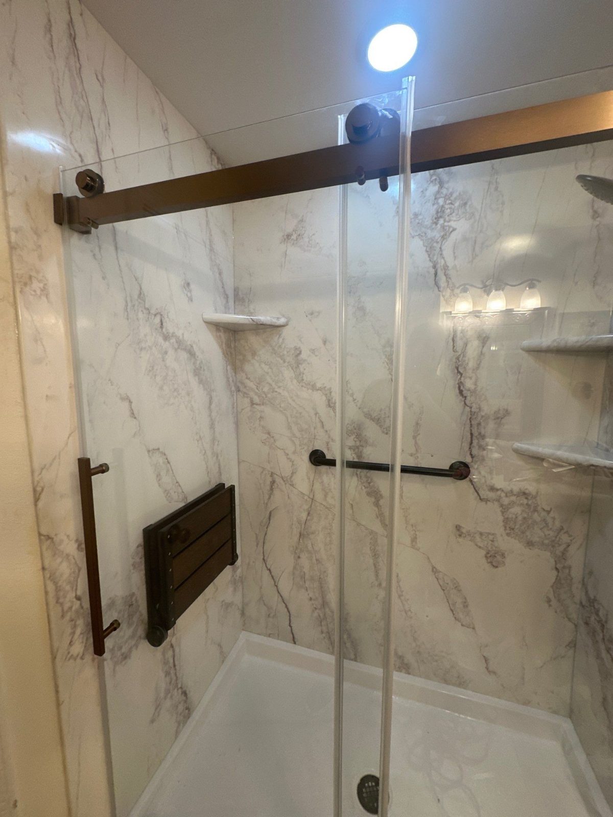Same Monterey shower after replacement with White Pearl marble-look walls, a barn-style glass door and a fold-up seat