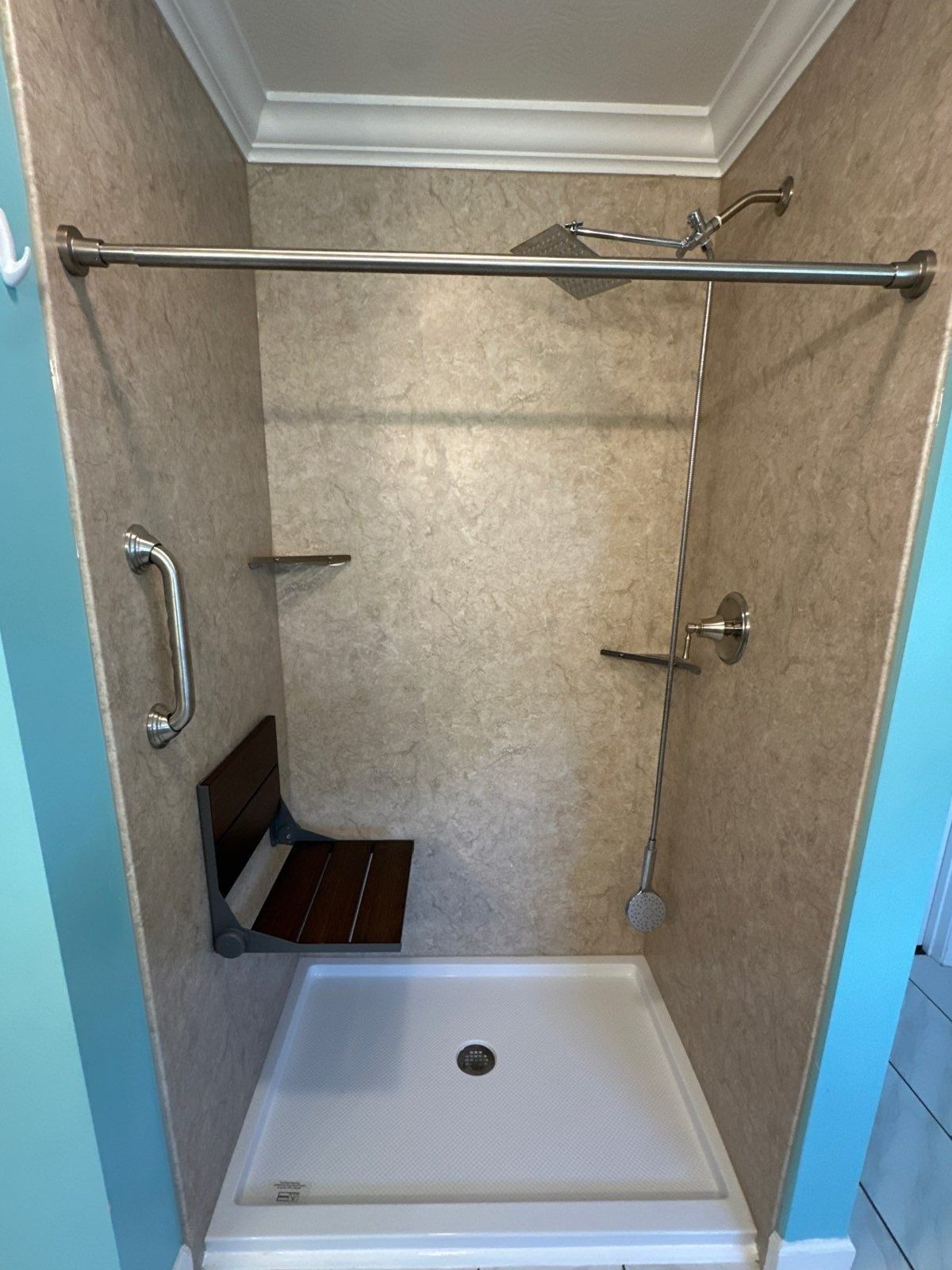 Same Rickman shower after replacement with Brecchia marble-look walls, a fold-up wood seat and a brushed nickel grab bar