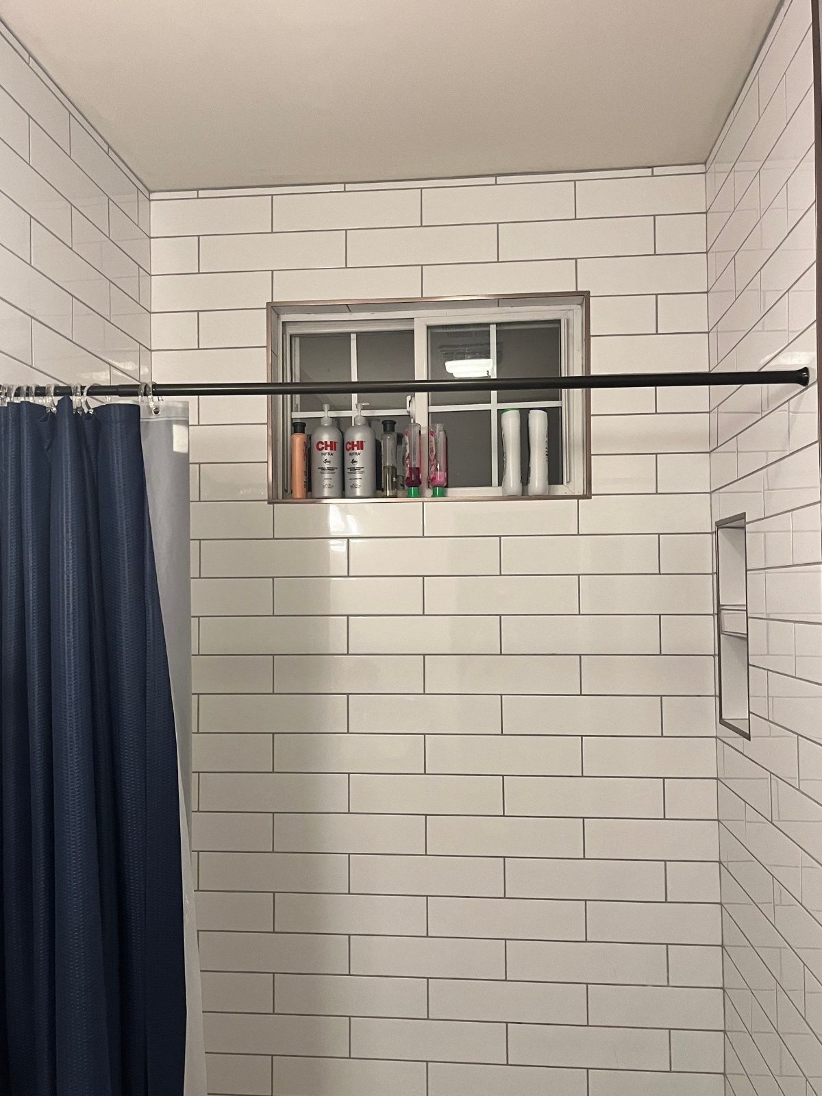 White subway tile tub surround with a window and a navy shower curtain before tub replacement in Cookeville, TN