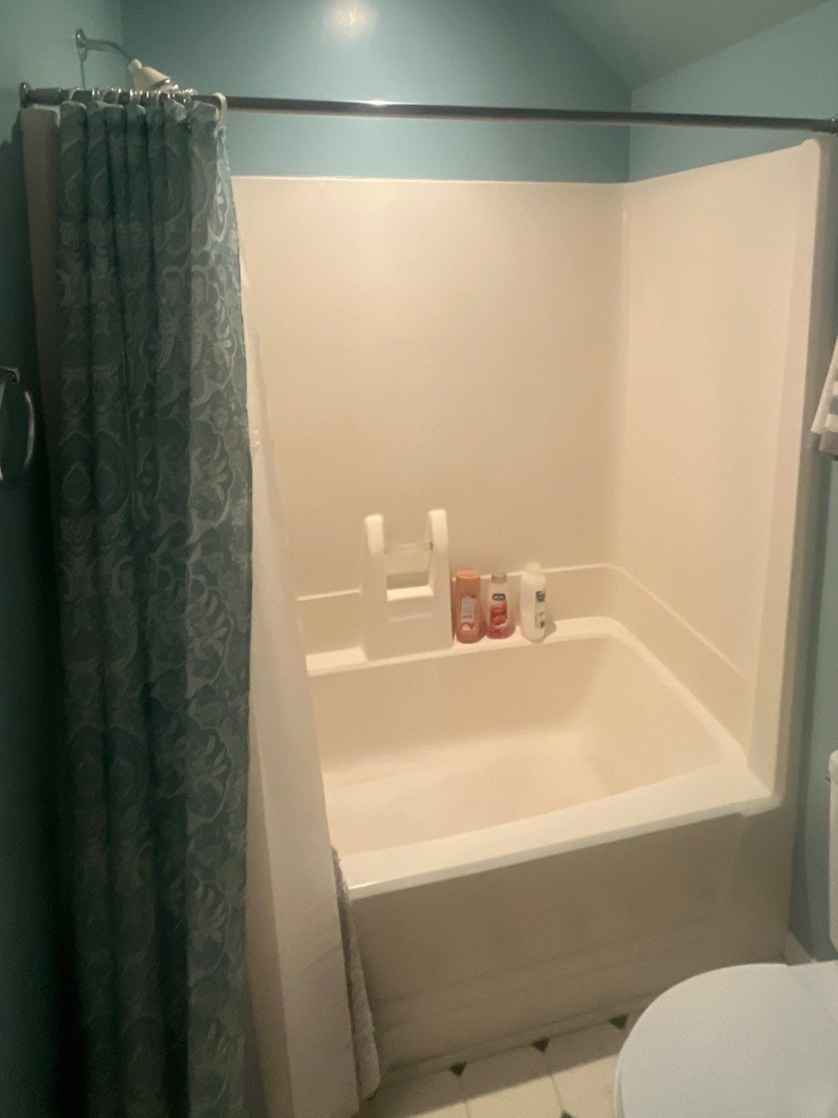 Almond fiberglass tub and shower unit with a patterned curtain under a sloped ceiling before replacement in Murfreesboro, TN