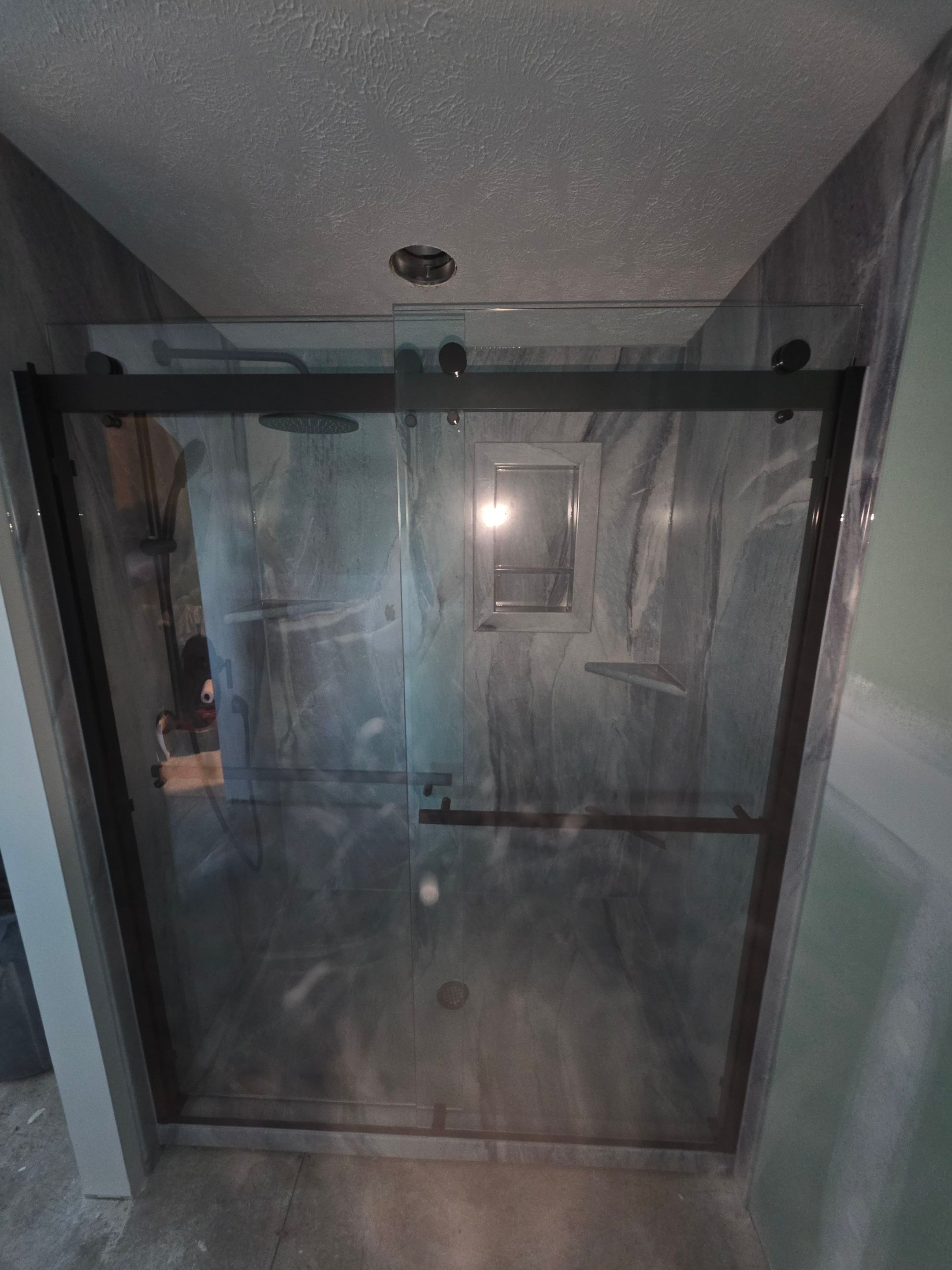 Same Gainesboro bathroom after shower installation with gray and white stone-look solid-surface walls, a recessed caddy, corner shelves and a dark-framed barn-style sliding glass door