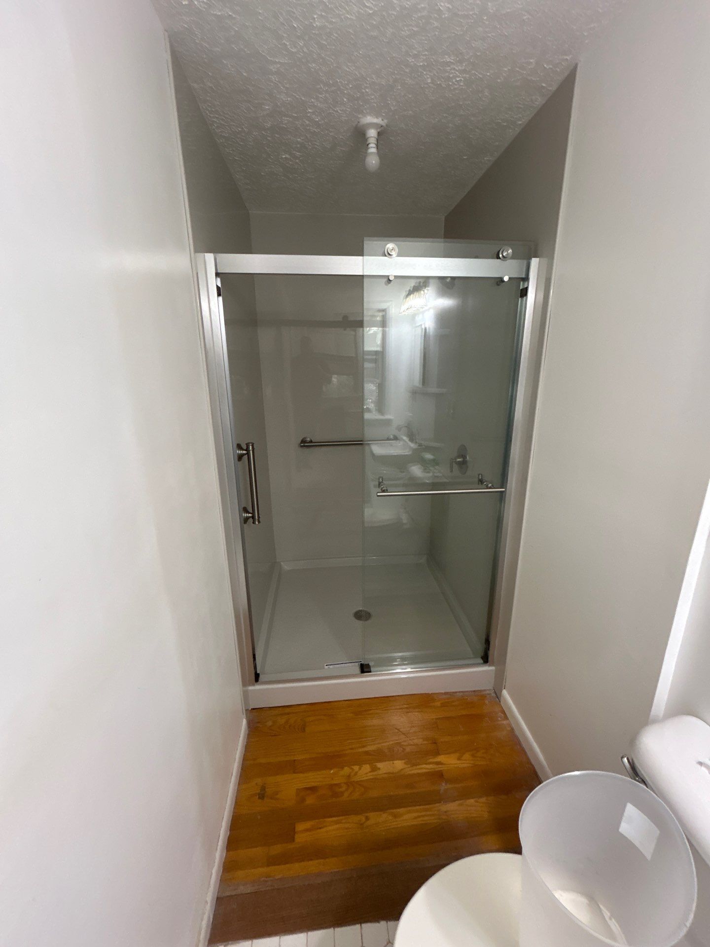Same Albany bathroom after shower replacement with smooth gray walls, a white low-profile base, an inside grab bar and a brushed nickel sliding glass door