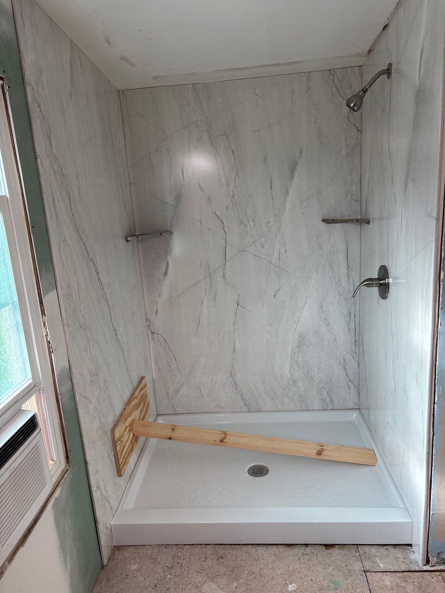 Same Pleasant View bathroom after shower replacement with white and gray veined marble-look walls, a white 40 by 54 inch base with center drain, brushed nickel shower head and lever valve, and two brushed nickel corner shelves