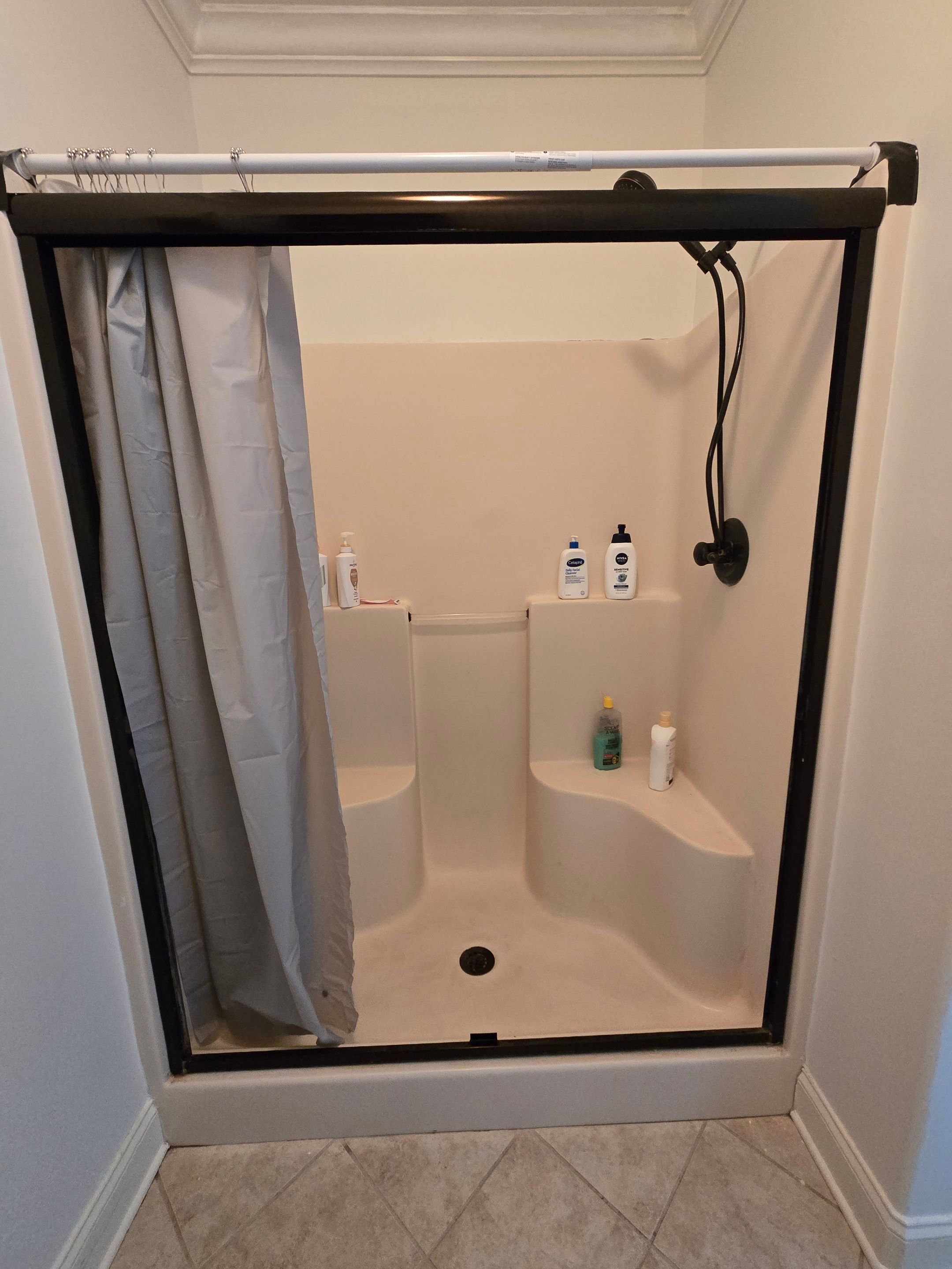 Old one-piece almond fiberglass shower with two molded corner seats, a dark-framed sliding door and a tension-rod curtain before shower replacement in Harvest, AL