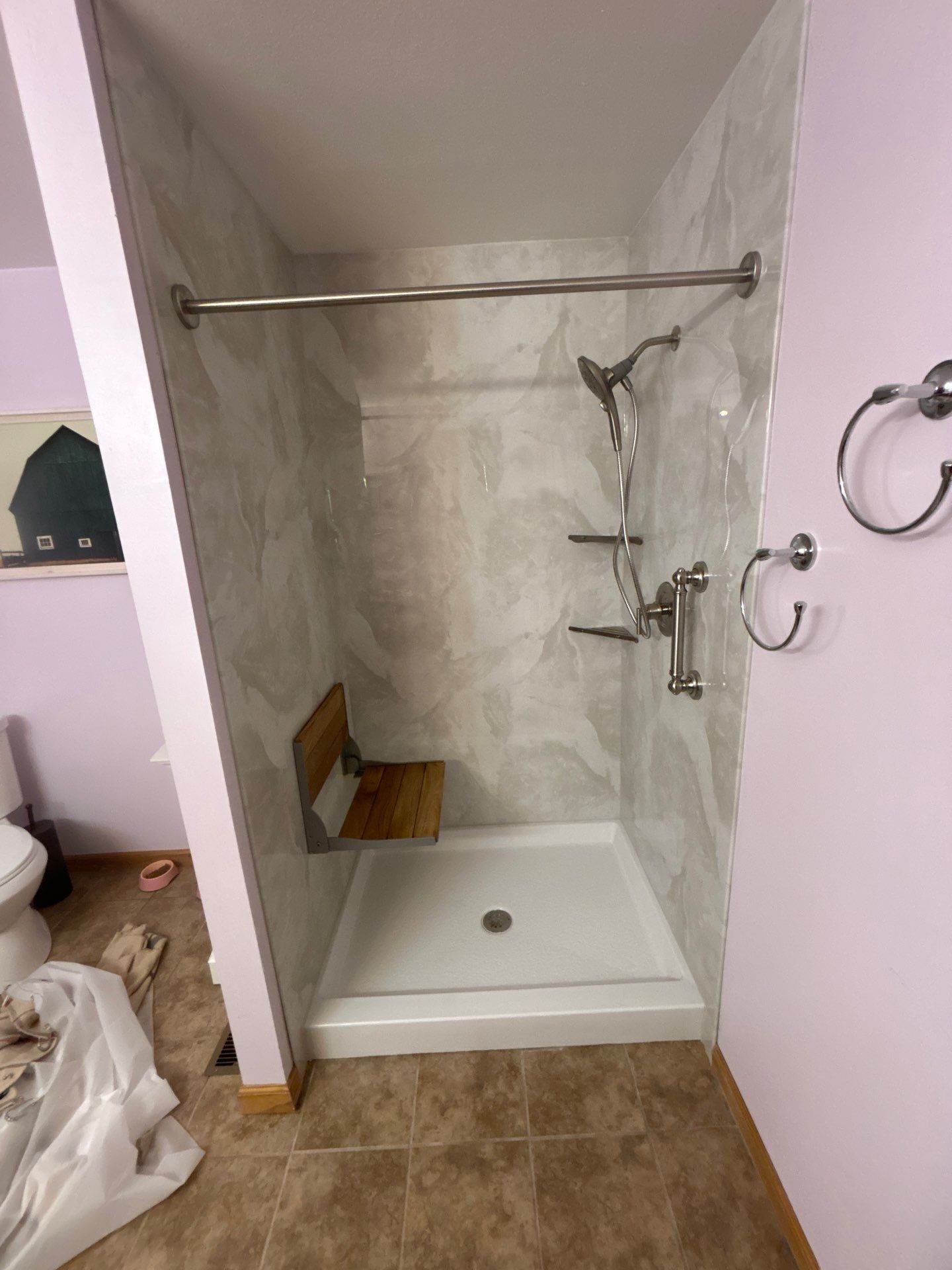 Same Celina bathroom after shower replacement with soft gray and white marble-look walls, a white base, teak fold-down seat, grab bar, brushed nickel handheld shower, corner shelves and curtain rod