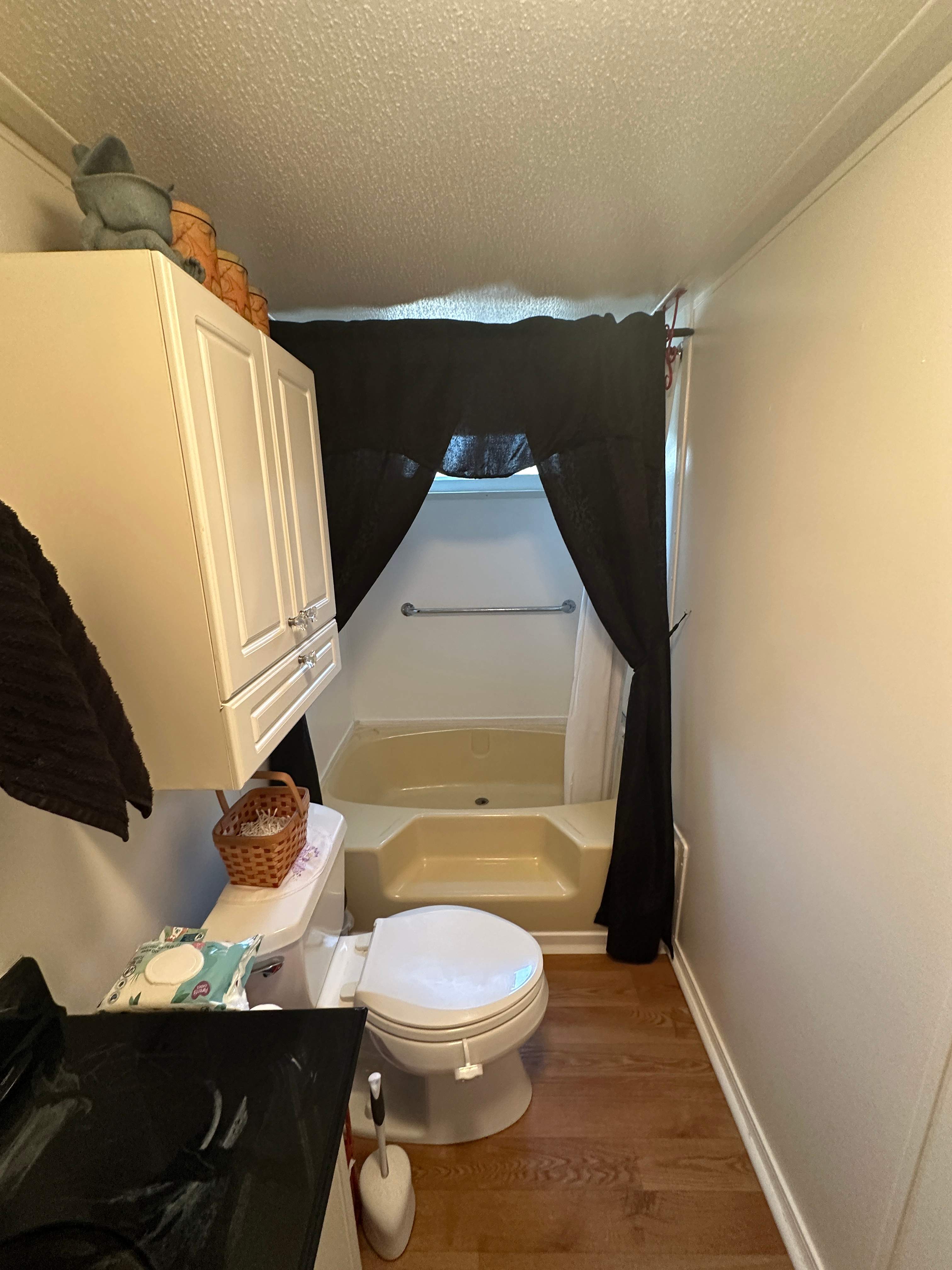 Narrow bathroom with an old almond tub, molded step, window above the tub and a dark fabric curtain before tub-to-shower conversion in Monroe, TN