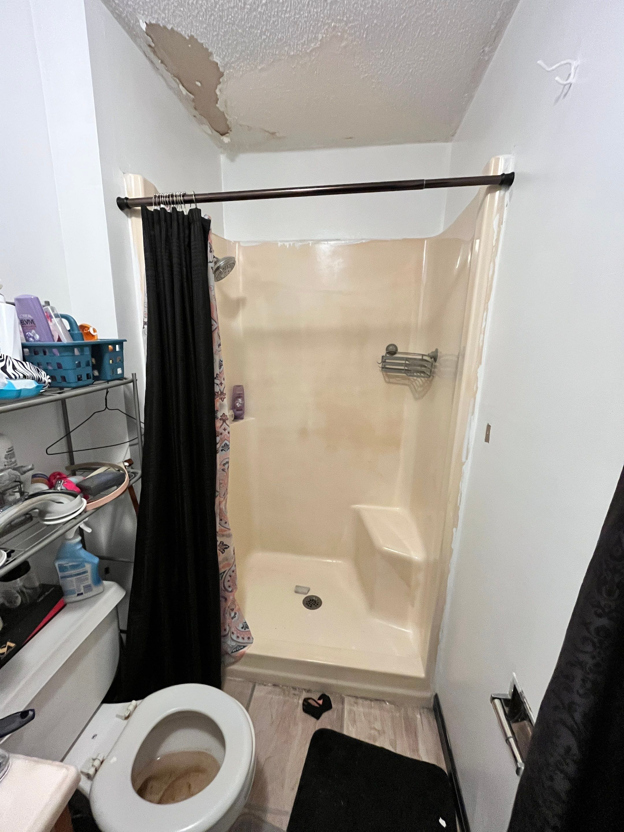 Stained almond fiberglass shower stall with a molded corner seat, wire caddy, bronze tension rod and dark curtain before shower replacement in Clarkrange, TN