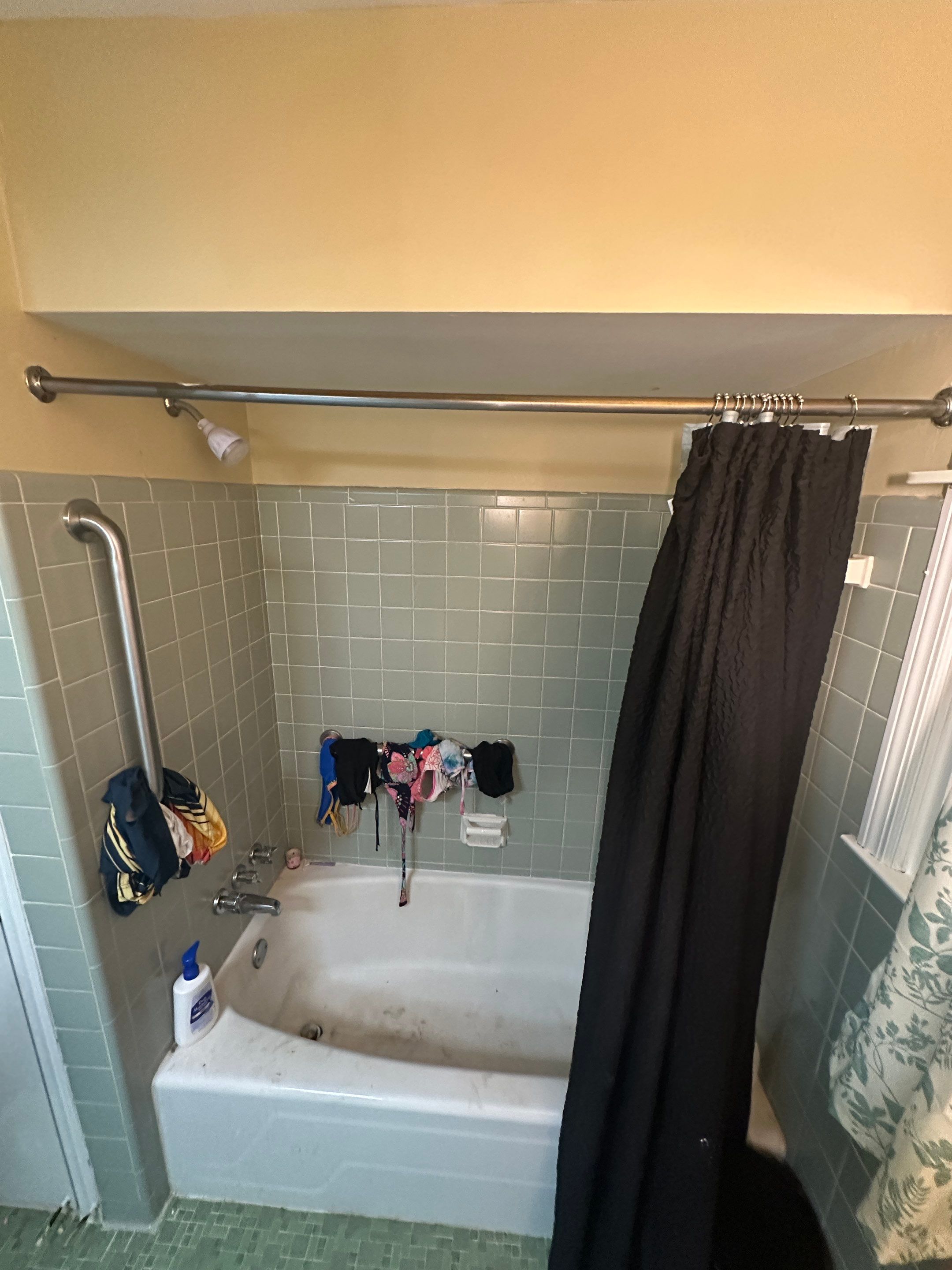 Worn white bathtub with stained finish, green ceramic tile surround, single grab bar and dark curtain before tub replacement in Columbia, TN