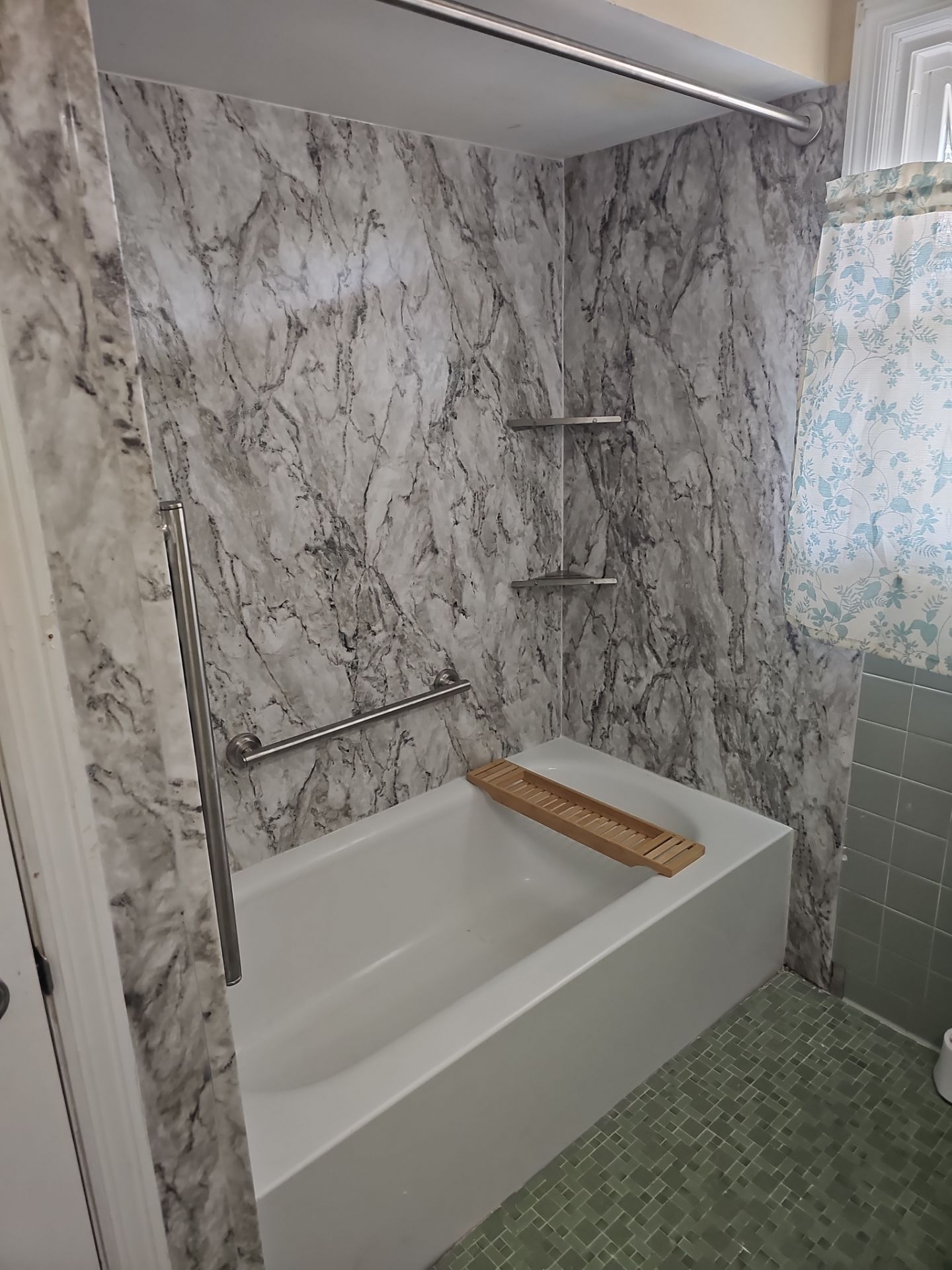 Same Columbia bathroom after tub replacement with a new white bathtub, gray-veined marble-look walls, two brushed nickel grab bars, metal corner shelves and a curtain rod