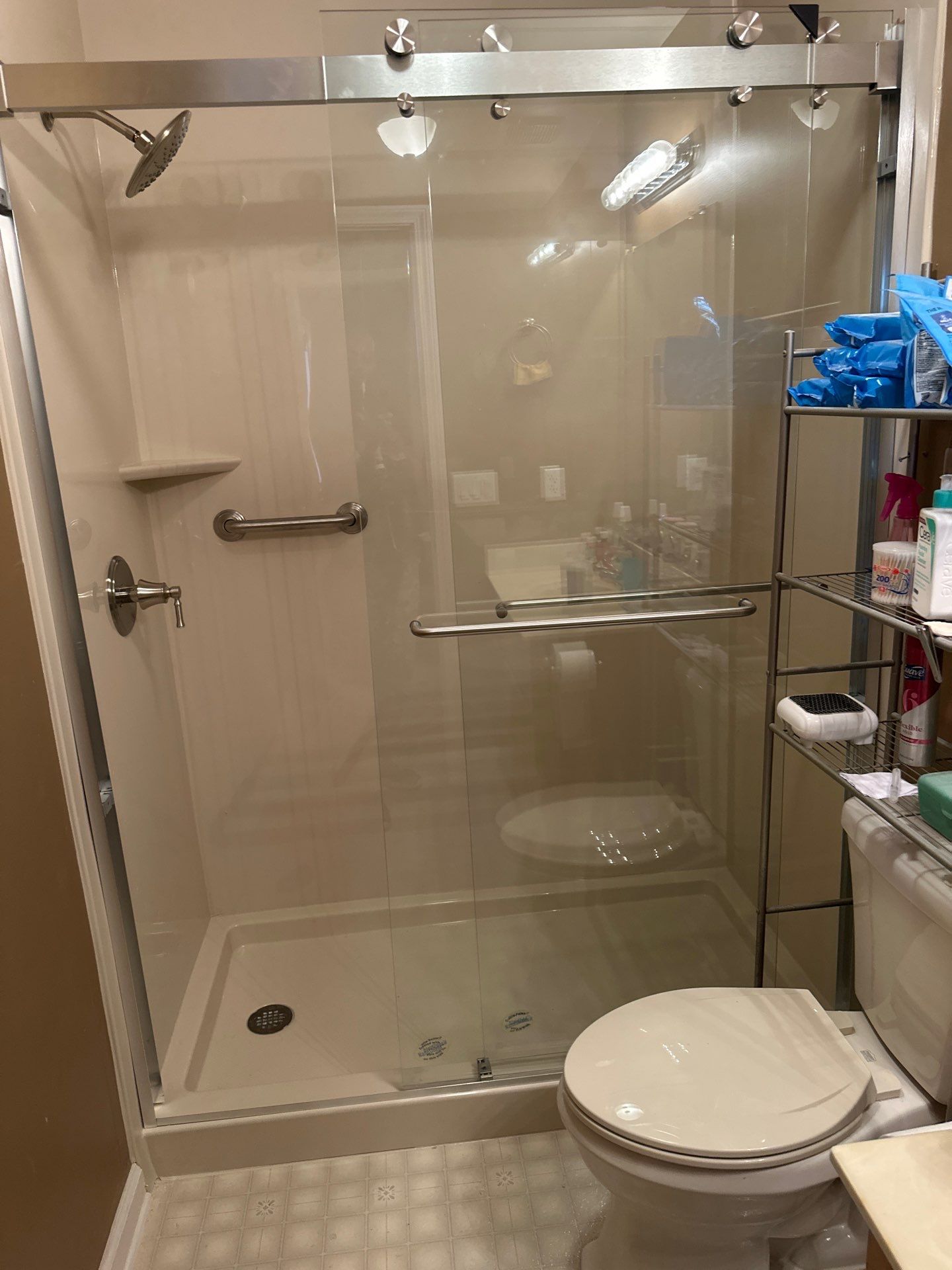 Same Columbia bathroom after tub-to-shower conversion with smooth beige walls, a low-threshold shower base, corner shelf, grab bar, brushed nickel fixtures and a clear sliding glass door