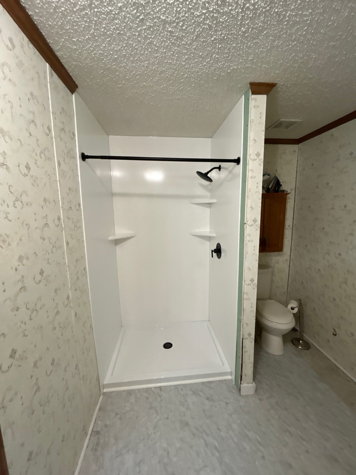 Same Moss bathroom after shower replacement with smooth solid white walls, a white shower base with center drain, three corner shelves, matte black shower head, valve and straight curtain rod