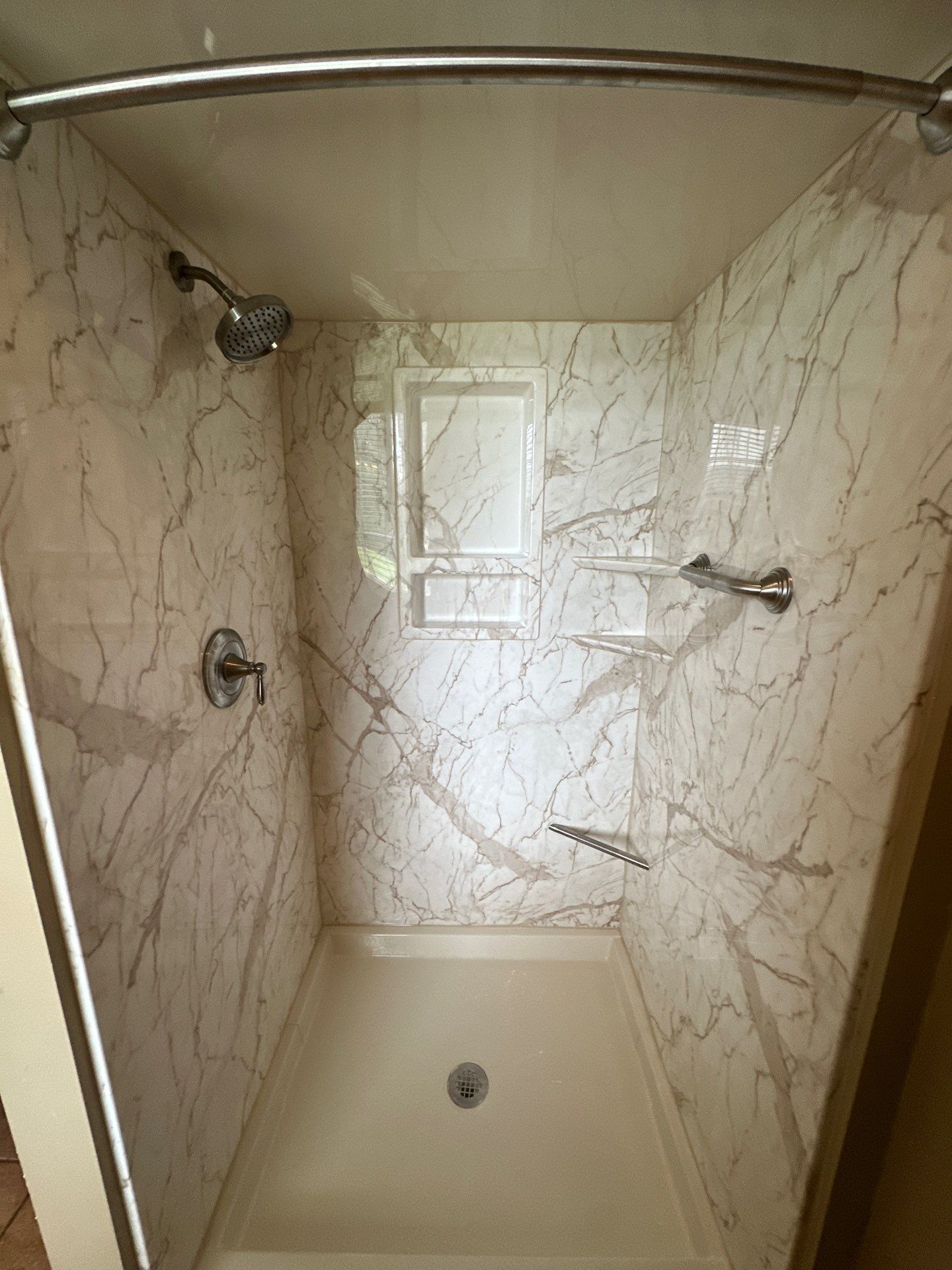 Same Morrison bathroom after shower replacement with white and taupe marble-look walls, a matching ceiling panel, recessed caddy, corner shelves, a foot pedestal, grab bar, brushed nickel fixtures and a curved curtain rod