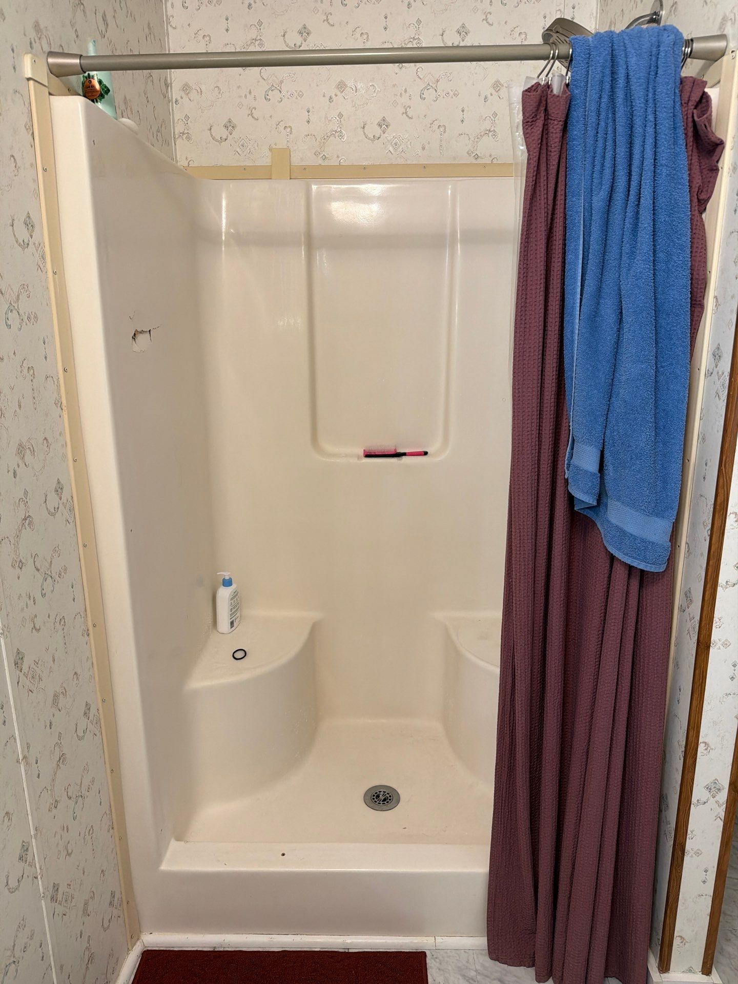 Old almond fiberglass shower stall with molded corner seats, a damaged side wall, tension rod and fabric curtain before shower replacement in Moss, TN