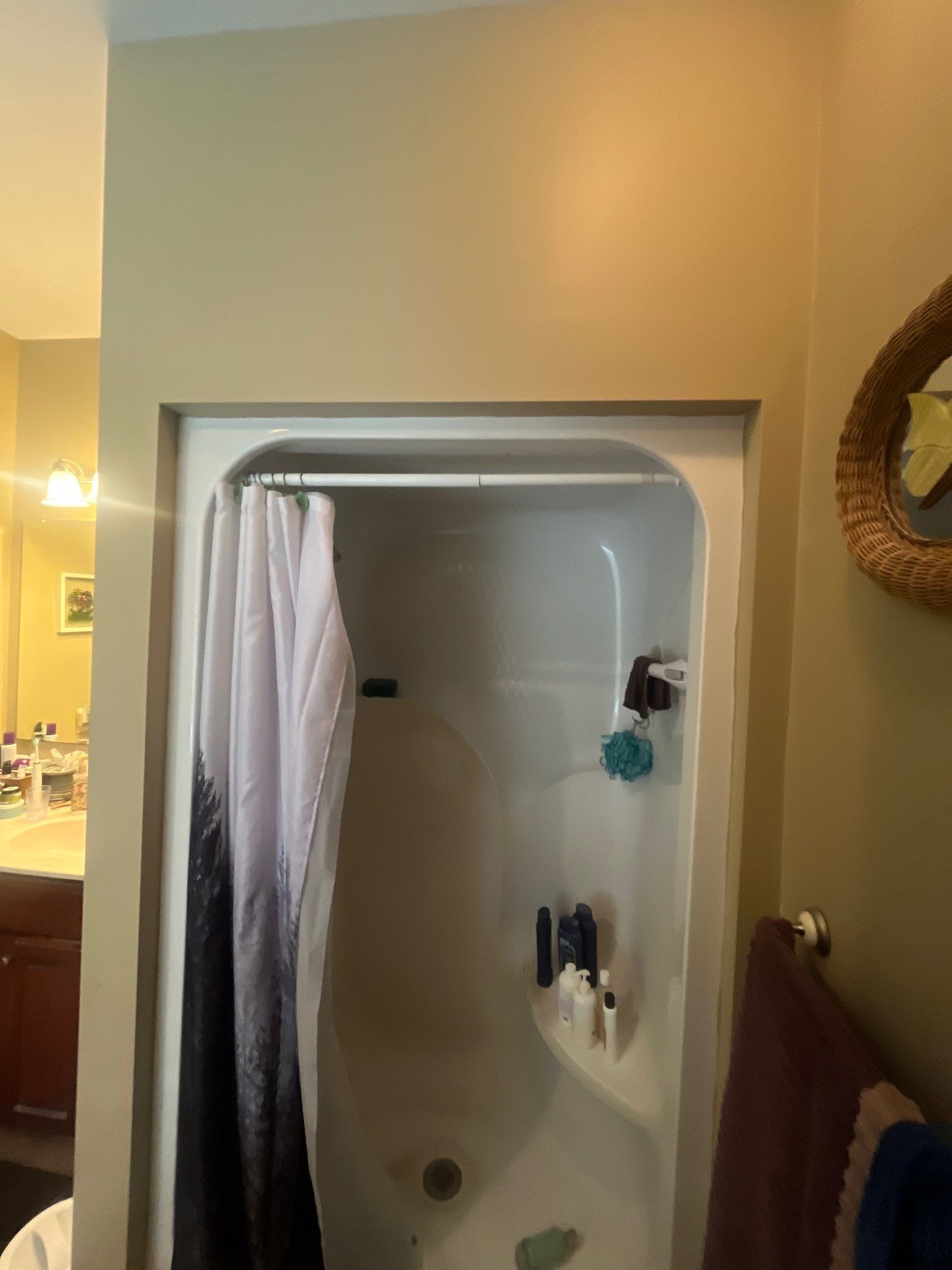 Old one-piece white fiberglass shower stall with molded corner shelf, tension rod and fabric curtain set into a framed alcove before shower replacement in Morrison, TN