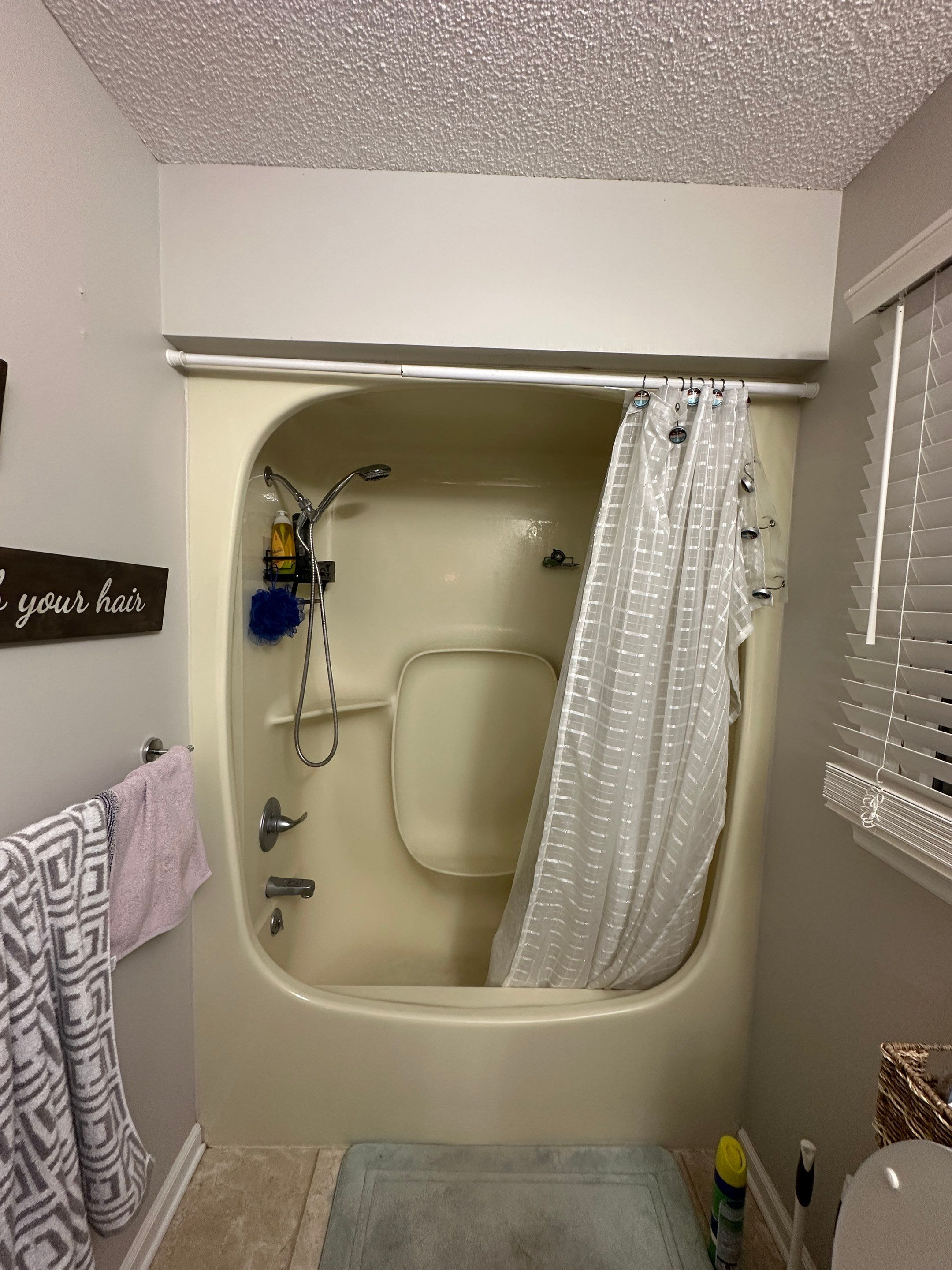 Almond one-piece fiberglass tub and shower with a molded seat bump, tension rod and curtain under a low soffit before tub-to-shower conversion in Winchester, TN