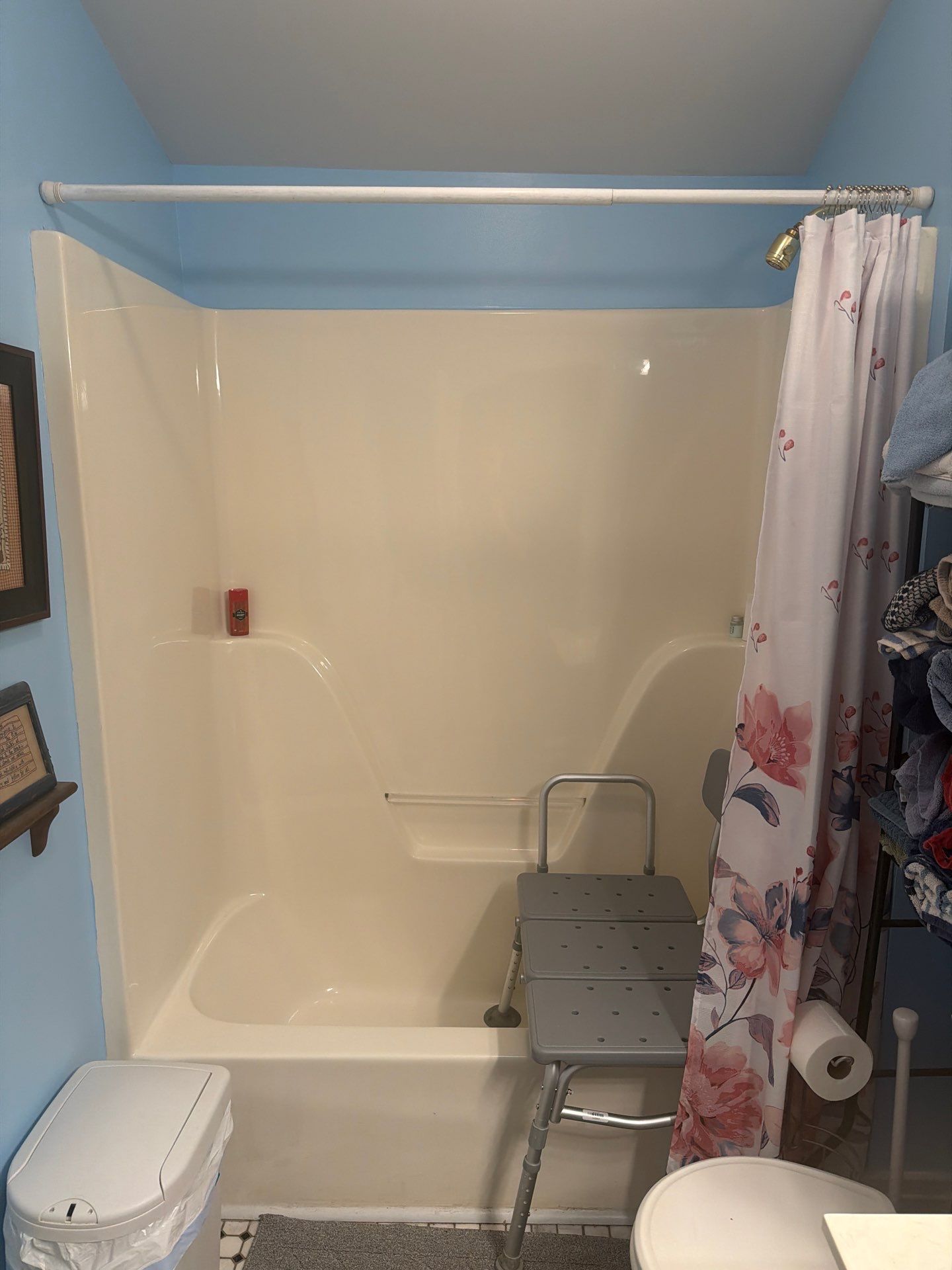 Almond one-piece fiberglass tub and shower with a tension curtain rod and a plastic transfer bench across the tub wall, under a sloped ceiling, before tub-to-shower conversion in Franklin, TN