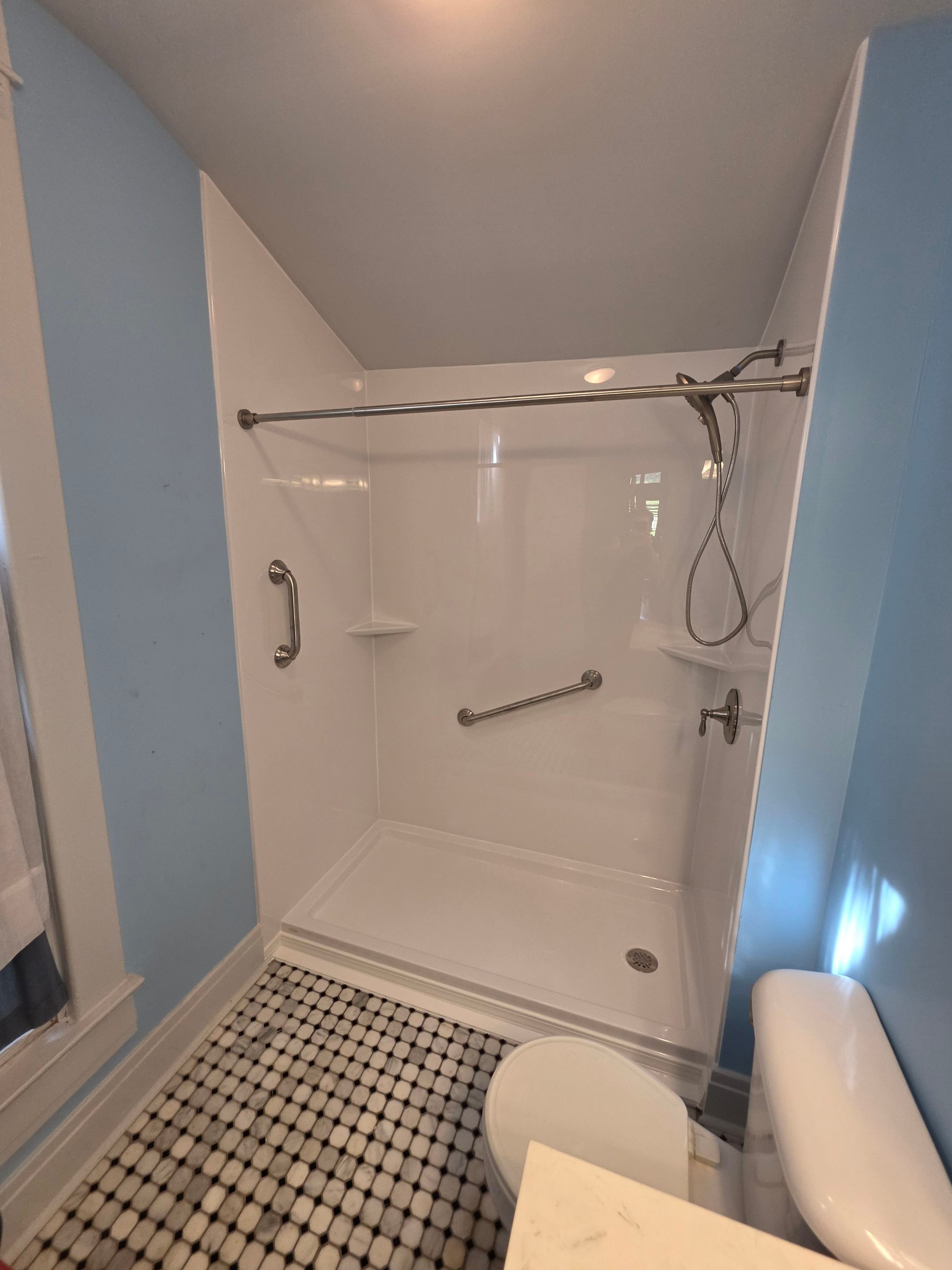 Same Franklin bathroom after tub-to-shower conversion with smooth white walls, a white 30" x 60" low-threshold shower base, two brushed nickel grab bars, a handheld shower on a hose, corner shelves and a brushed nickel curtain rod