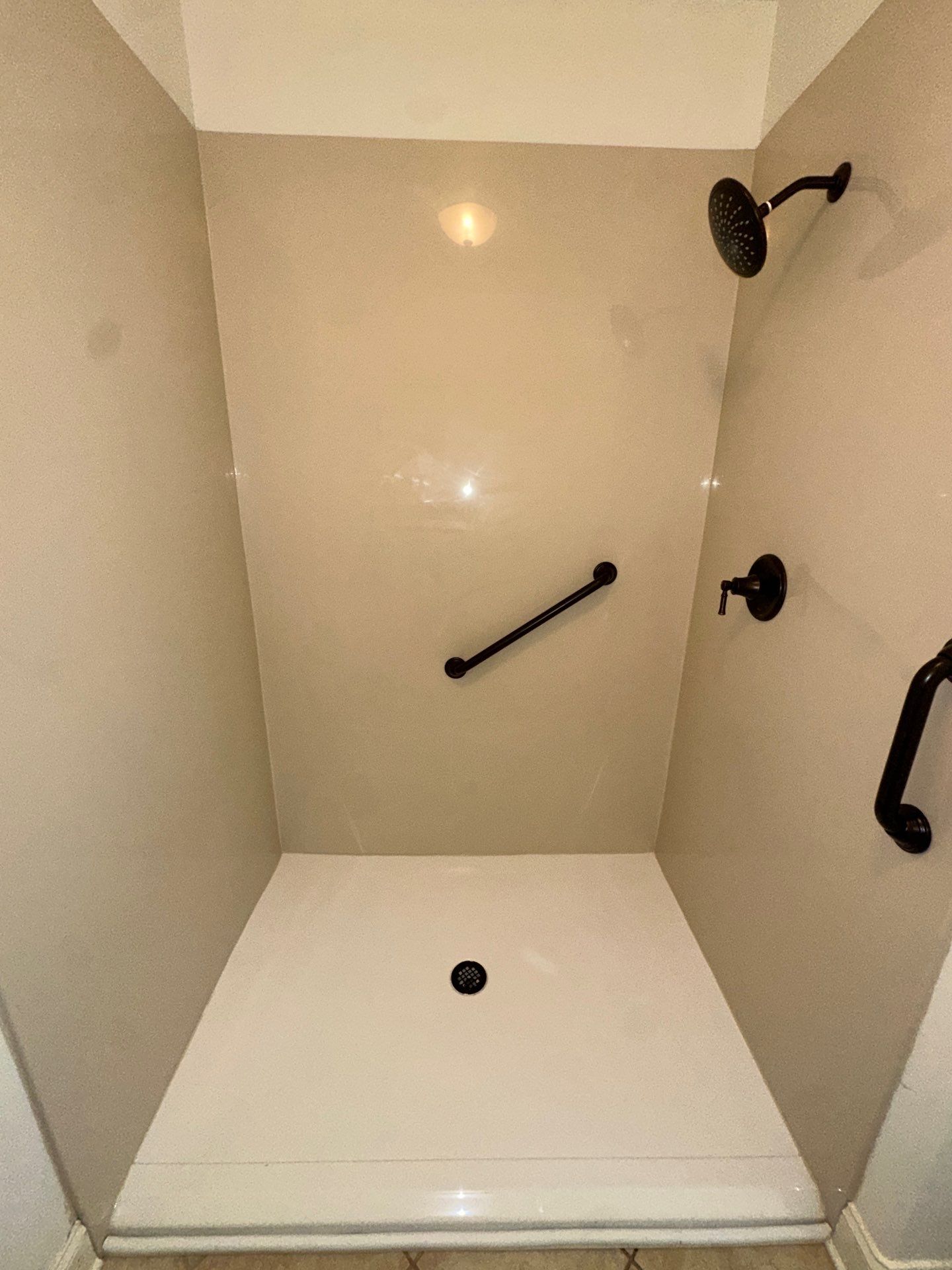 Same Harvest bathroom after shower replacement with smooth beige solid walls, a white low-threshold shower base, oil-rubbed bronze fixtures and two bronze grab bars