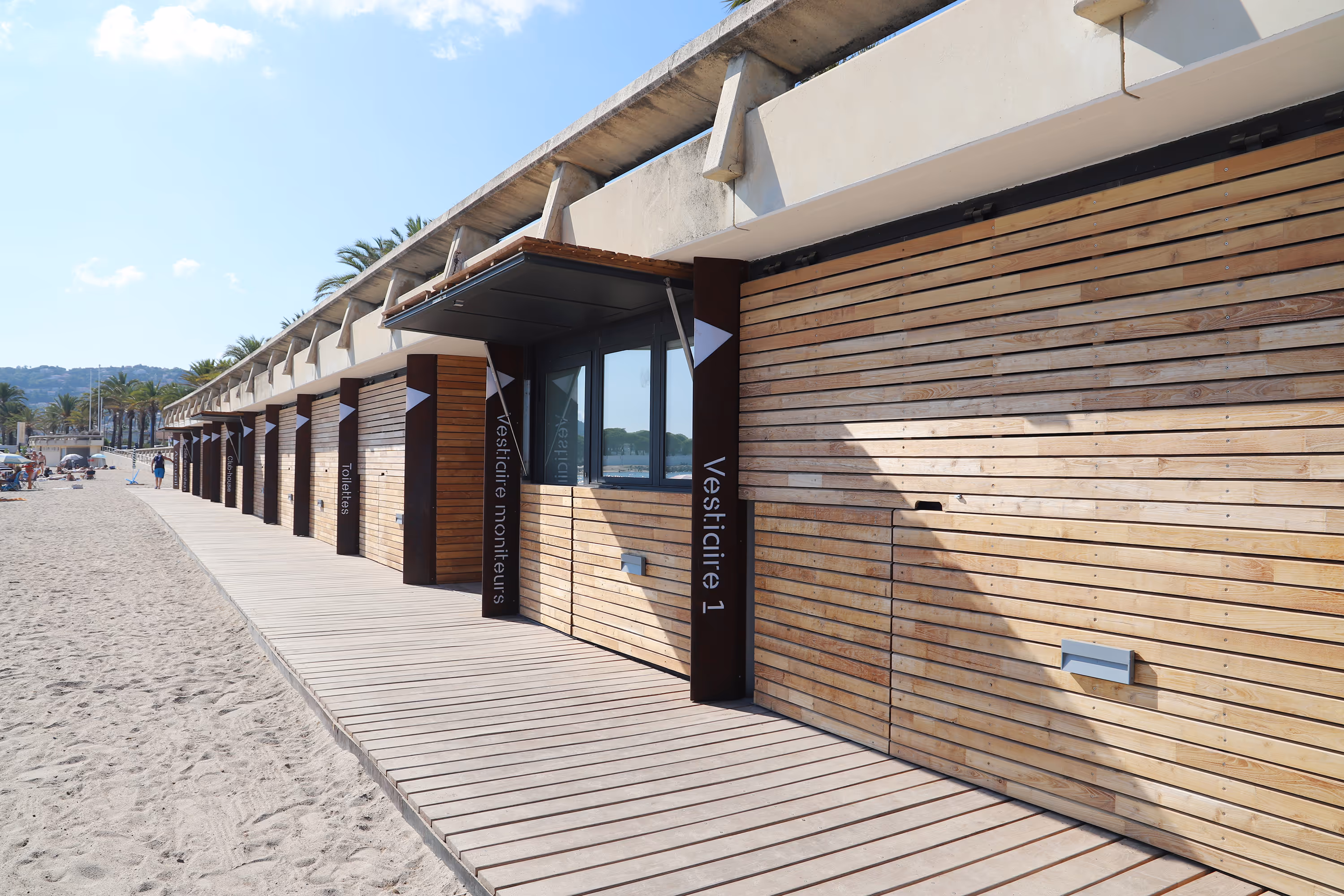 Base nautique en bardage bois avec volet rabattable sur verrins au-dessus des fenêtres pour refermer totalement la façade la nuit