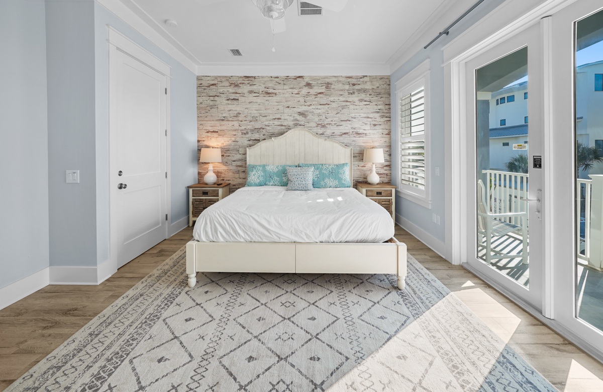 Coastal bedroom with king bed, balcony doors, and wood accent wall