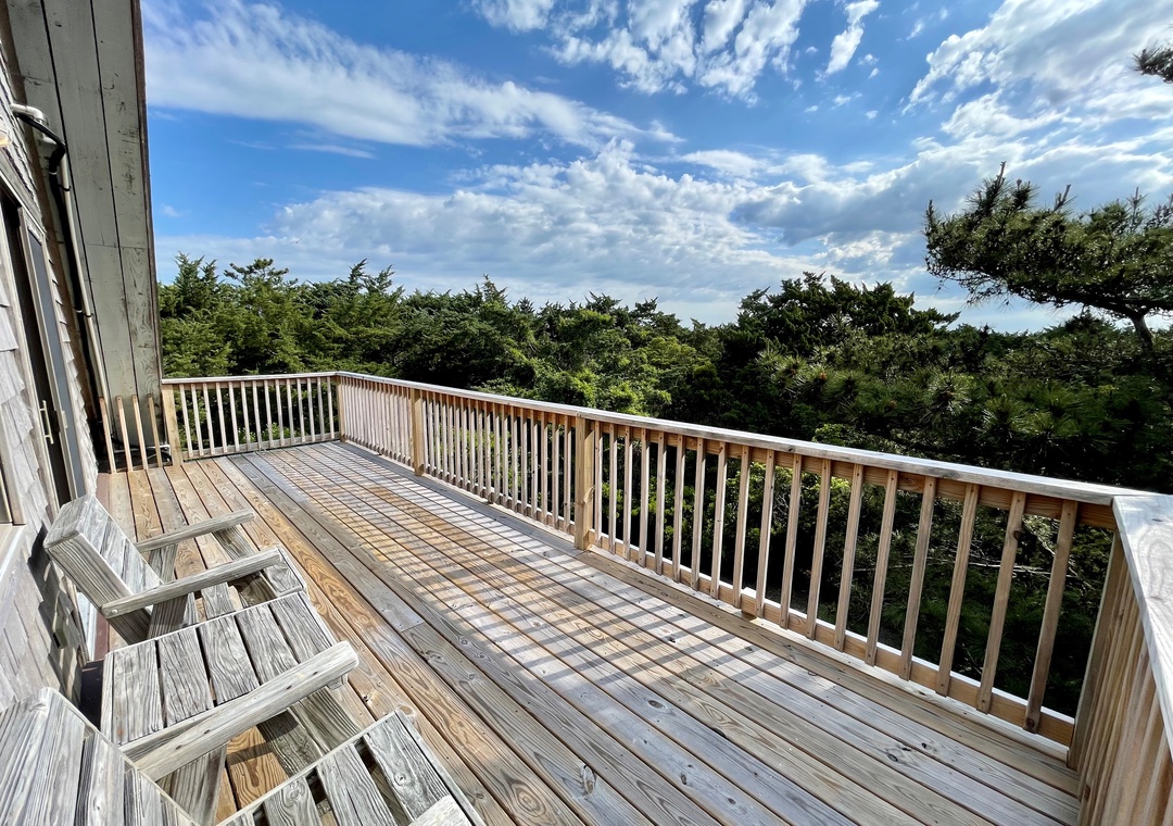 Top-level wooden deck with two chairs and a tree-lined view under a blue sky