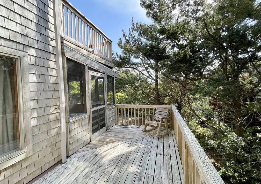 Outdoor wooden deck beside the house with a single rocking chair overlooking trees