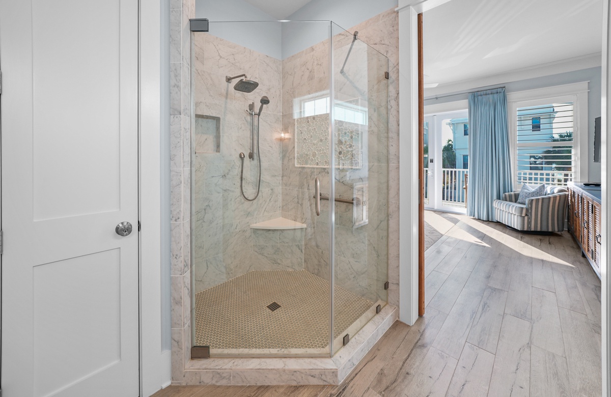 Glass walk-in shower with marble tile beside coastal bedroom with balcony