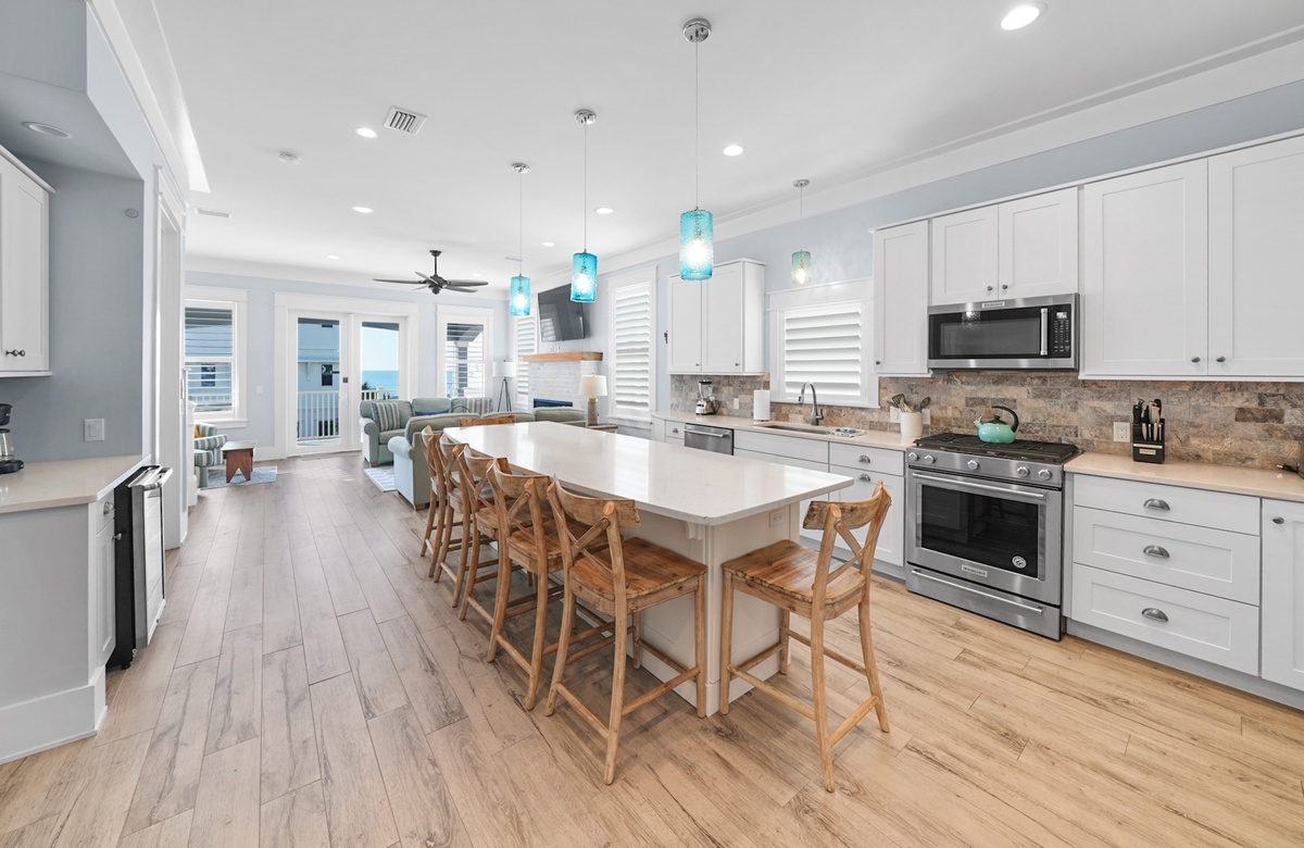 Open coastal kitchen with large island, pendant lights, and ocean-view living room