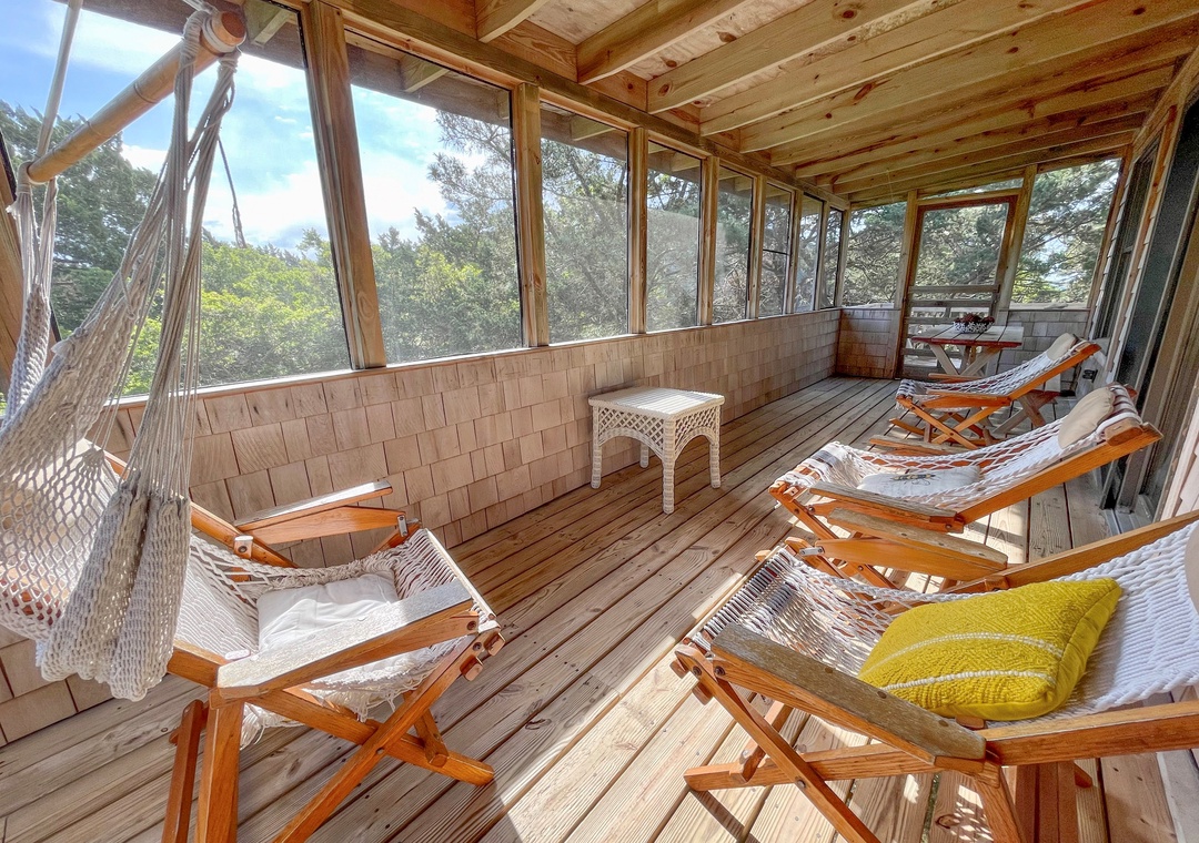 Screened-in porch with wood floors, hammock-style chairs, small tables, and views of surrounding trees