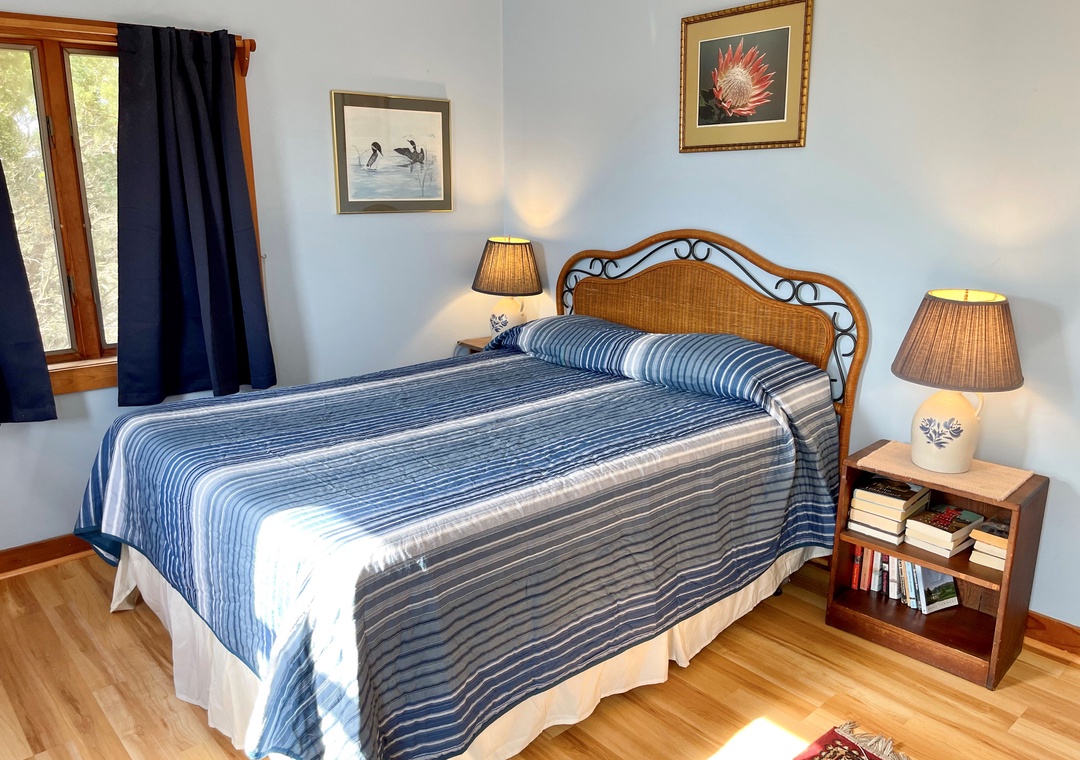 Bedroom with a queen bed, blue striped bedspread, wicker headboard, light blue walls, and two nightstands with lamps