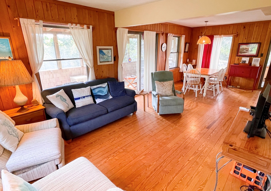 Open living and dining room with wood floors, two sofas, chairs, a dining table, and plenty of windows with curtains