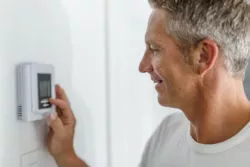 Homeowner adjusting thermostat on white wall.
