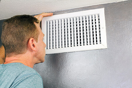 Person looking inside an air vent near the ceiling.