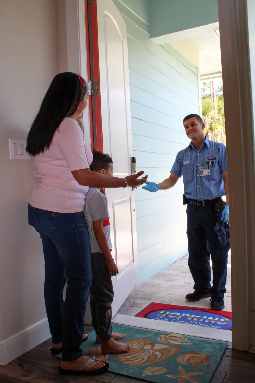 A woman and child greet a HVAC technician at the front door of their home.