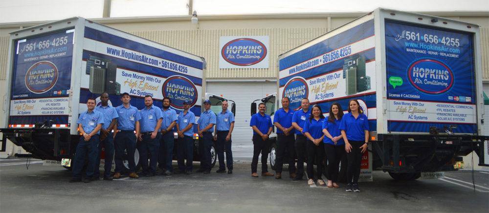 Hopkins Air Conditioning employees standing between two large Hopkins service trucks