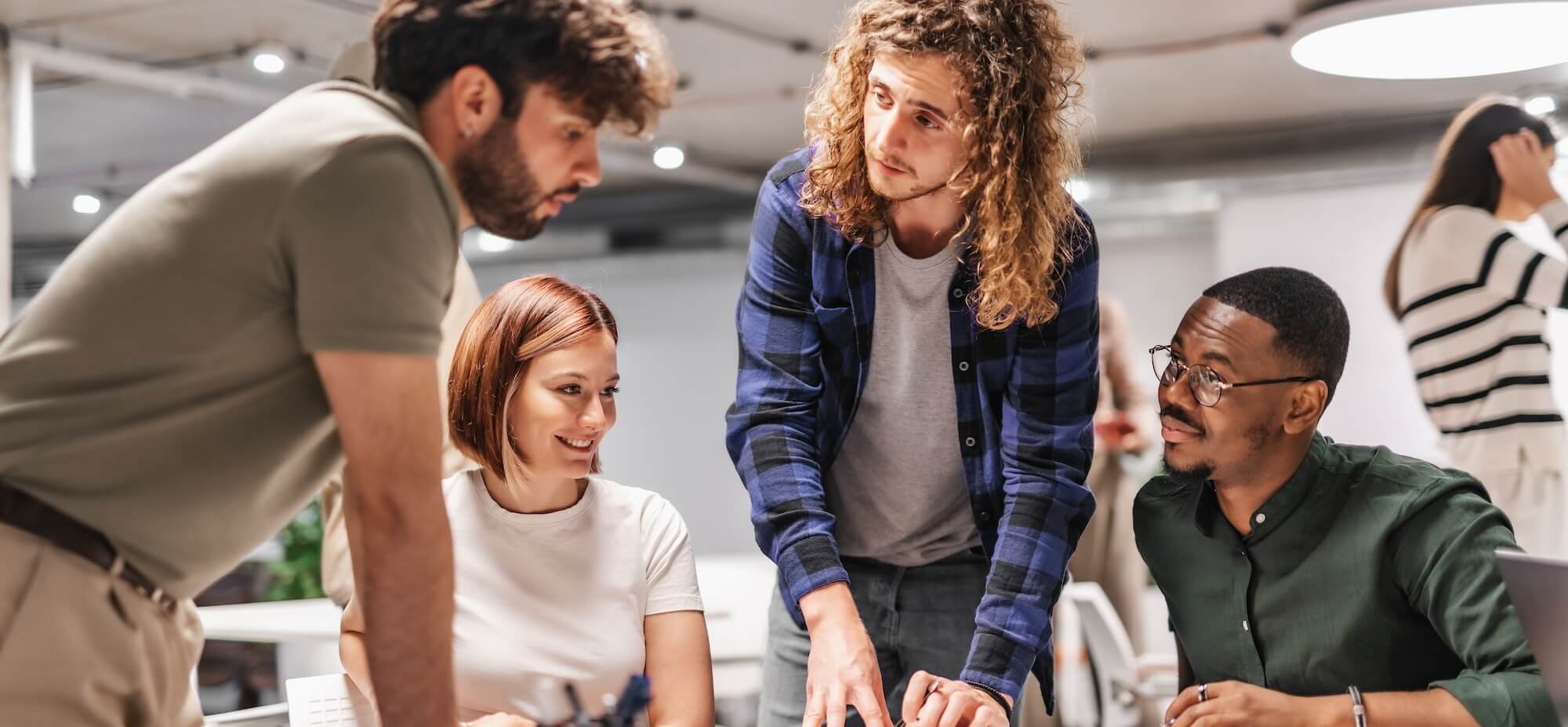 Four diverse colleagues collaborating and discussing work around a desk in a modern office.