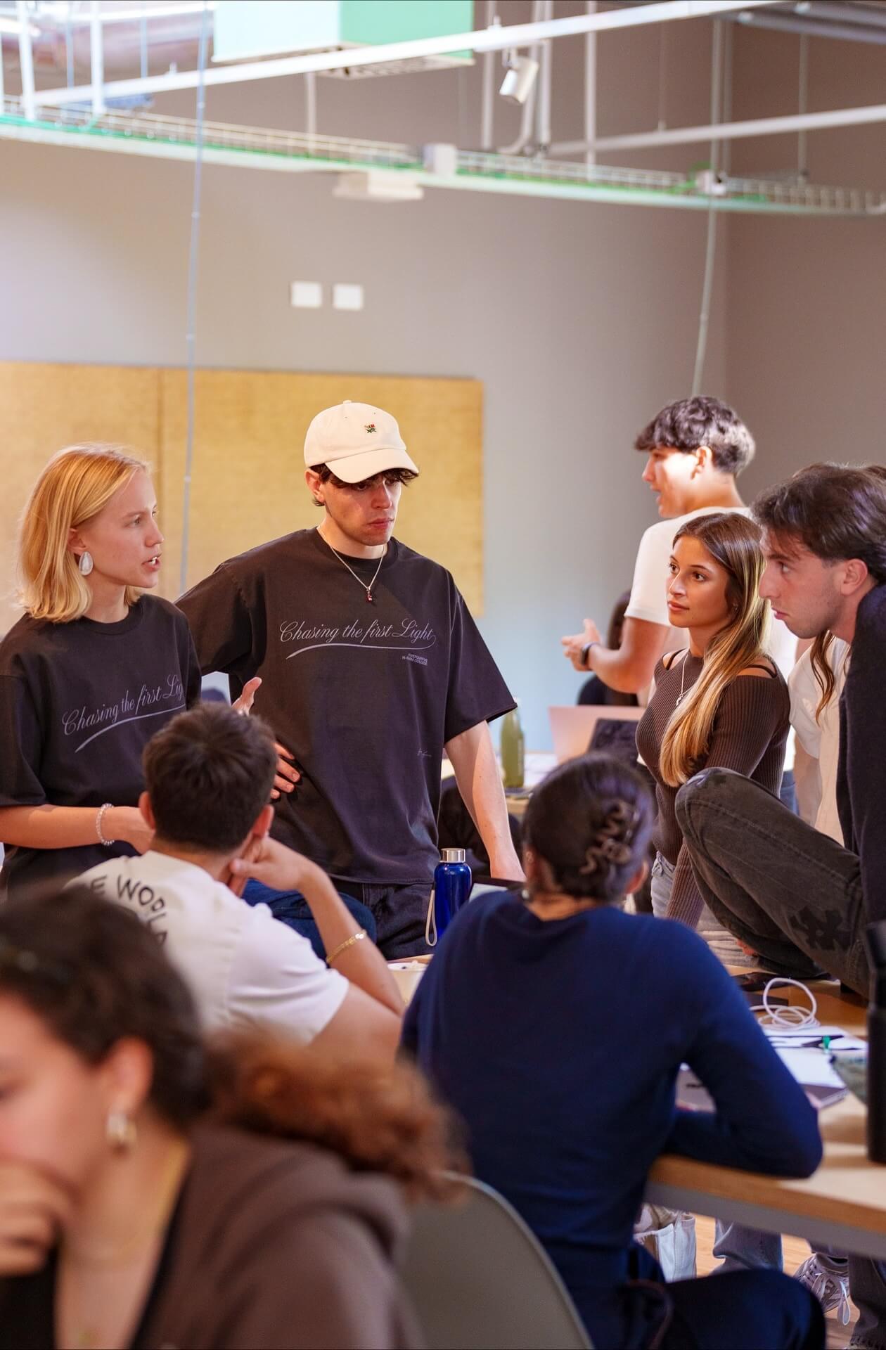 Group of young adults engaged in a serious discussion in a casual indoor setting around a table.