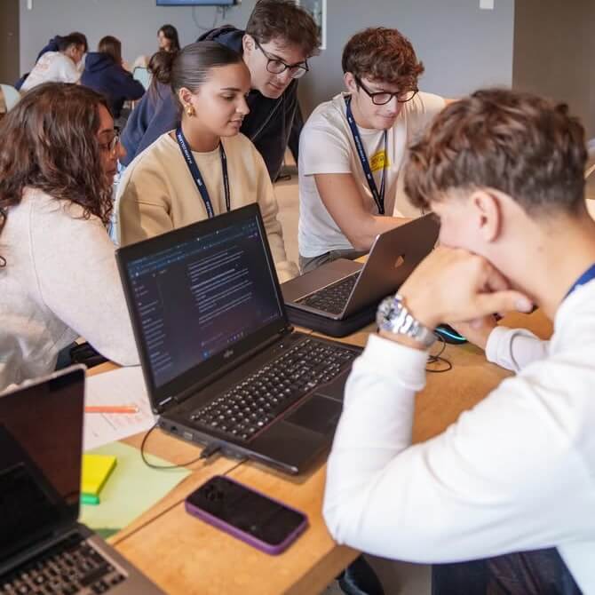 A group of young adults sitting around a table working collaboratively on laptops in a casual setting.