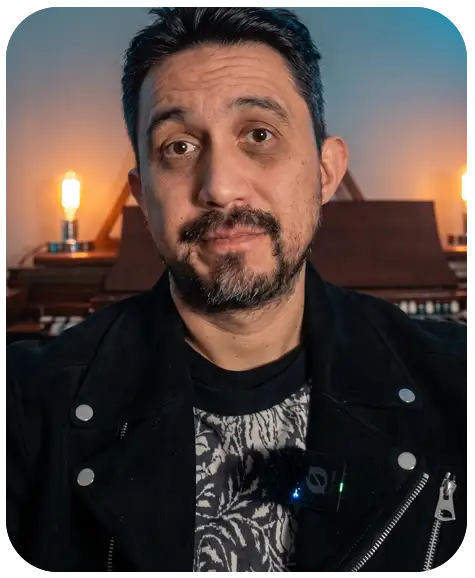Hombre con barba y pelo corto oscuro, fondo rojo, expresión facial seria con leve sonrisa.