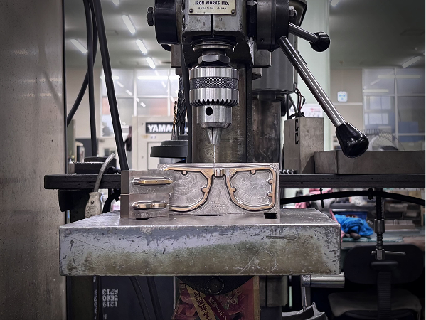 A custom-engraved brass mold for DRK eyewear, showing its intricate detailing, set in a high-precision milling machine at the Sabae factory.