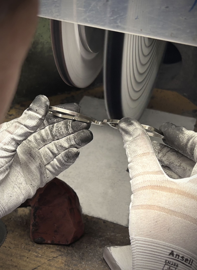 An artisan's gloved hands, stained from work, skillfully hand-polishing a DRK frame on a high-speed buffing wheel to create a flawless, luxury finish.