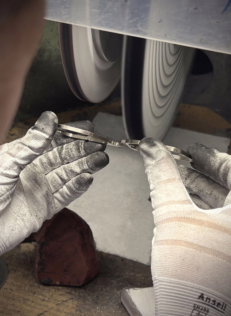 An artisan's gloved hands, stained from work, skillfully hand-polishing a DRK frame on a high-speed buffing wheel to create a flawless, luxury finish.
