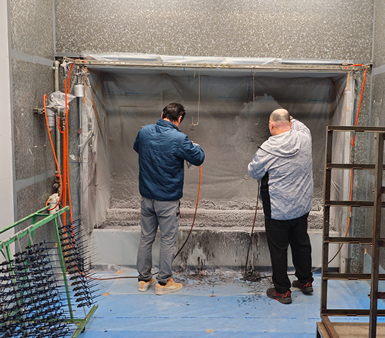 Two artisans in a specialized industrial booth, applying a meticulous, high-performance coating to DRK frames, which are racked nearby awaiting the finishing process.