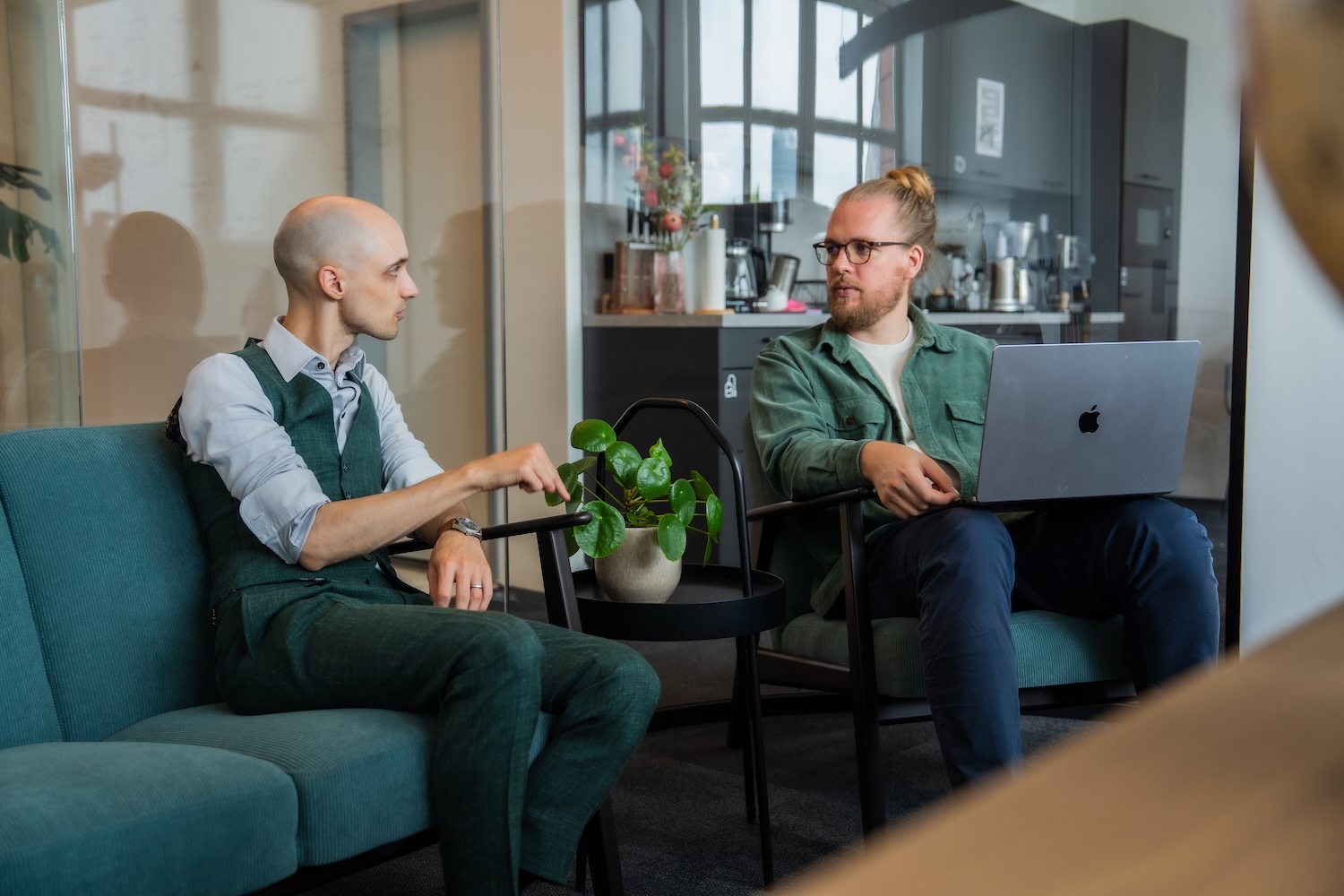 Two seated people talking, one taking notes on a computer