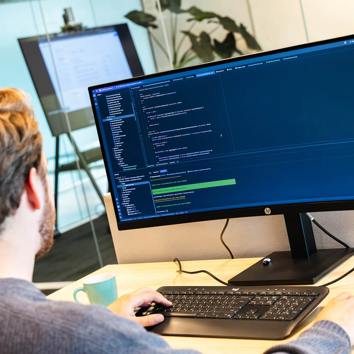 Man die in een kantooromgeving een groot computerscherm bekijkt met zichtbare programmatuur en code.