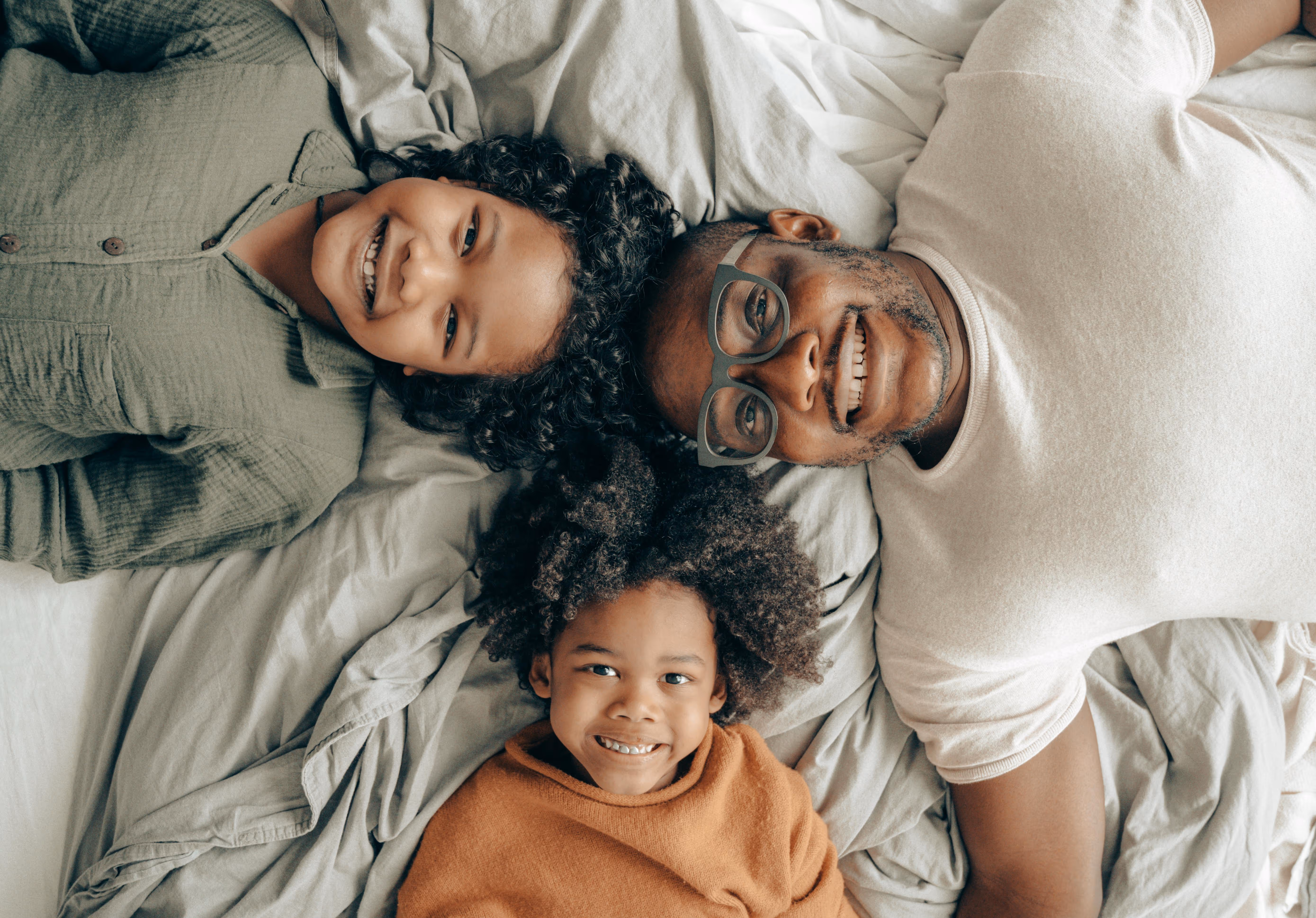 Smiling father and two children lying on a bed looking up at the camera.