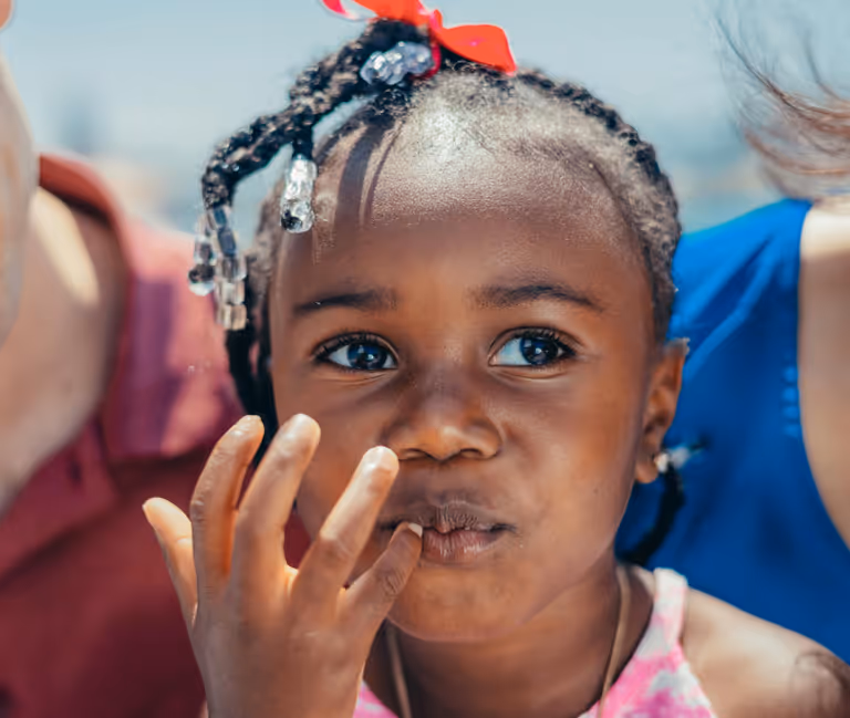 Young girl with braided hair decorated with beads and a red bow.