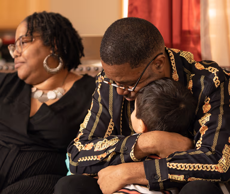 Man wearing patterned shirt embraces a child.