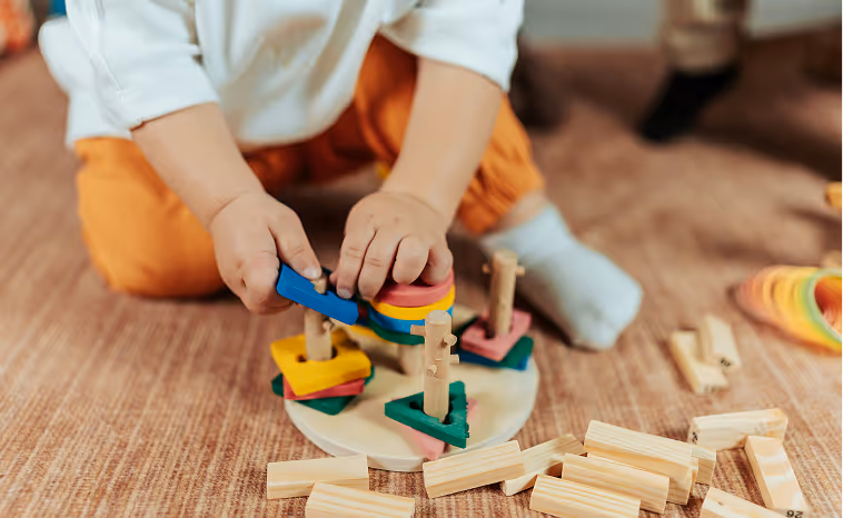 Child playing with colorful wooden shape sorting toy on a brown carpet.