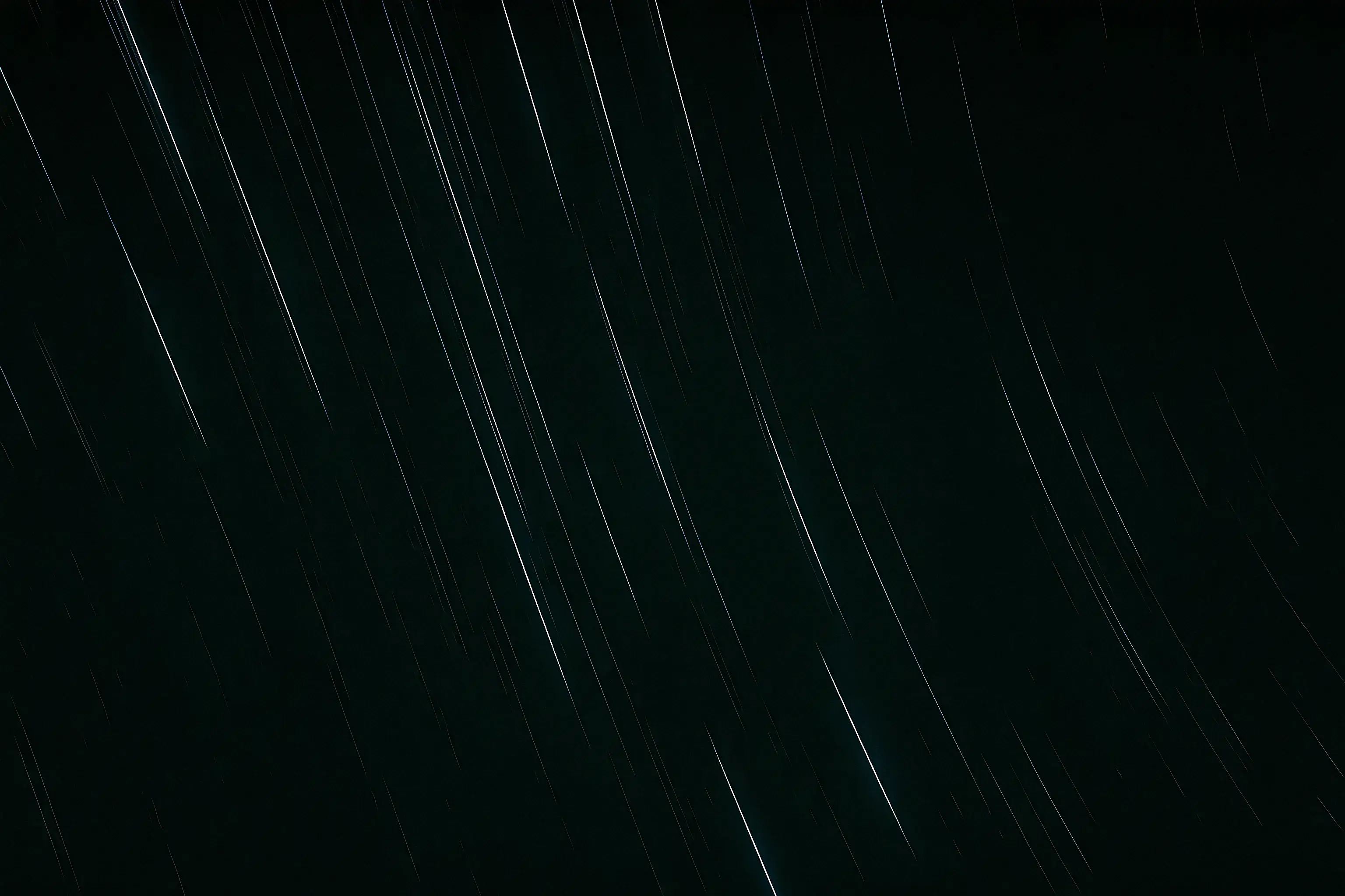 Long-exposure photo of star trails streaking diagonally across a dark night sky.
